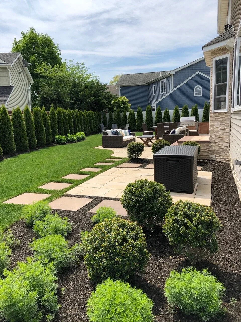 Backyard landscaping with patio paths, outdoor seating areas, and privacy plantings in Melville, NY