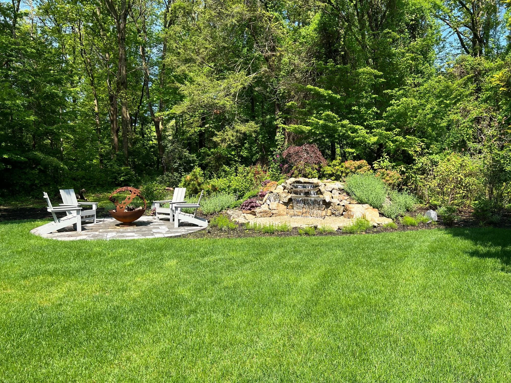 Natural backyard pond with layered stone waterfall and surrounding greenery in Stony Brook, NY