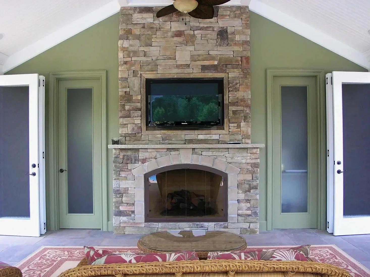 A wood-burning outdoor fireplace with stone surround and integrated media wall in Setauket, NY