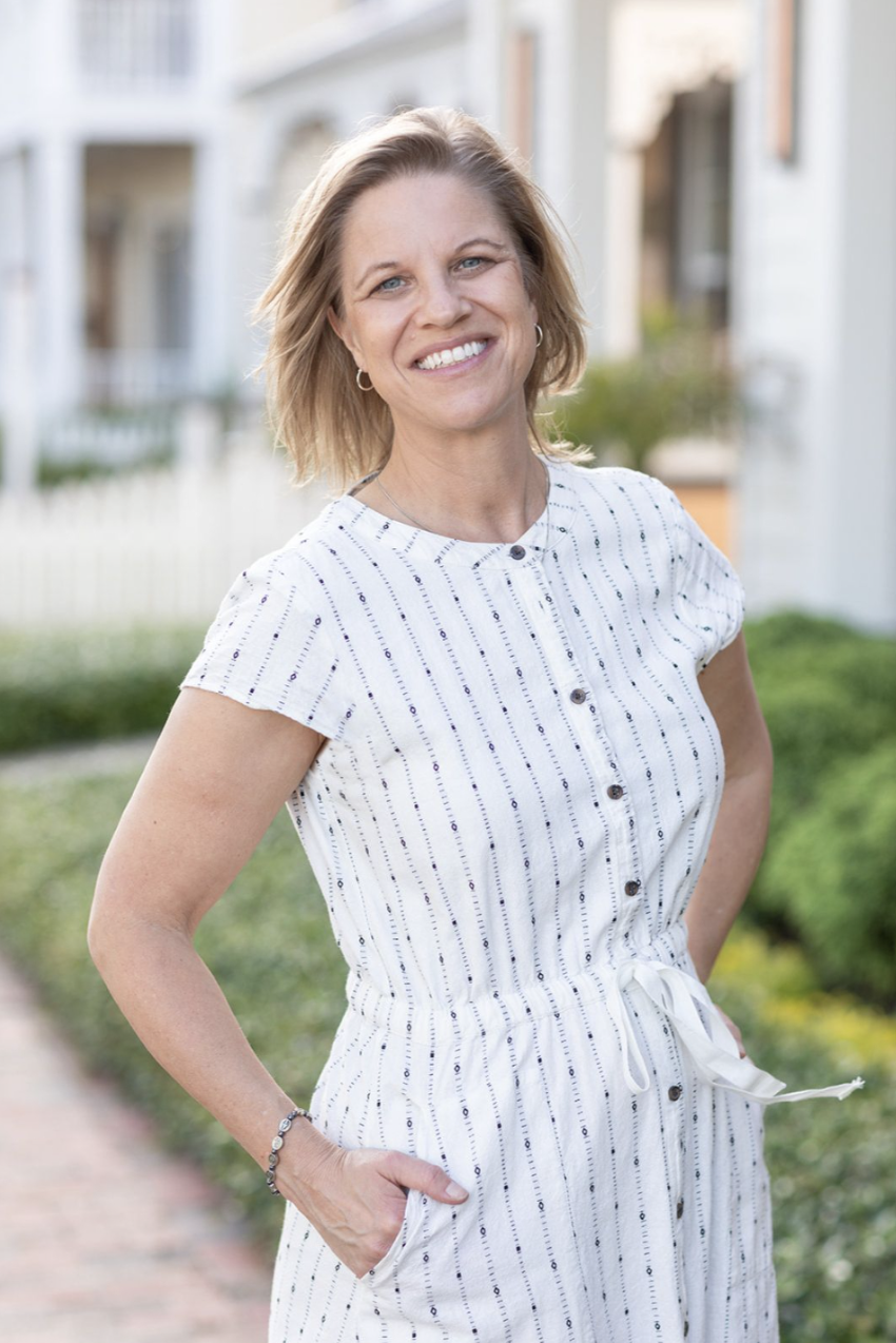 Smiling woman in a white striped dress standing outdoors on a sidewalk with houses in the background.
