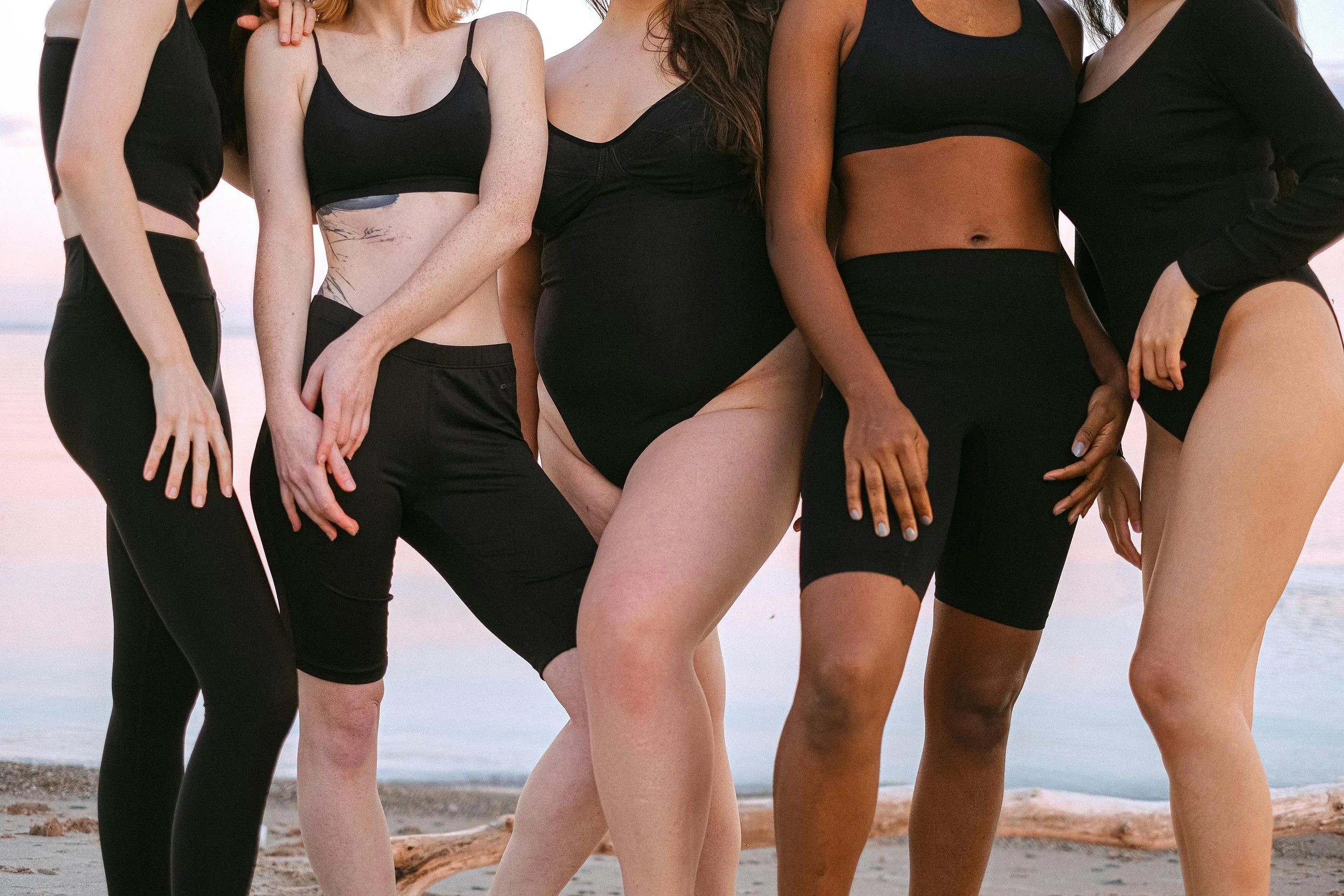 Group of women in athletic wear standing on a beach, with ocean in the background.