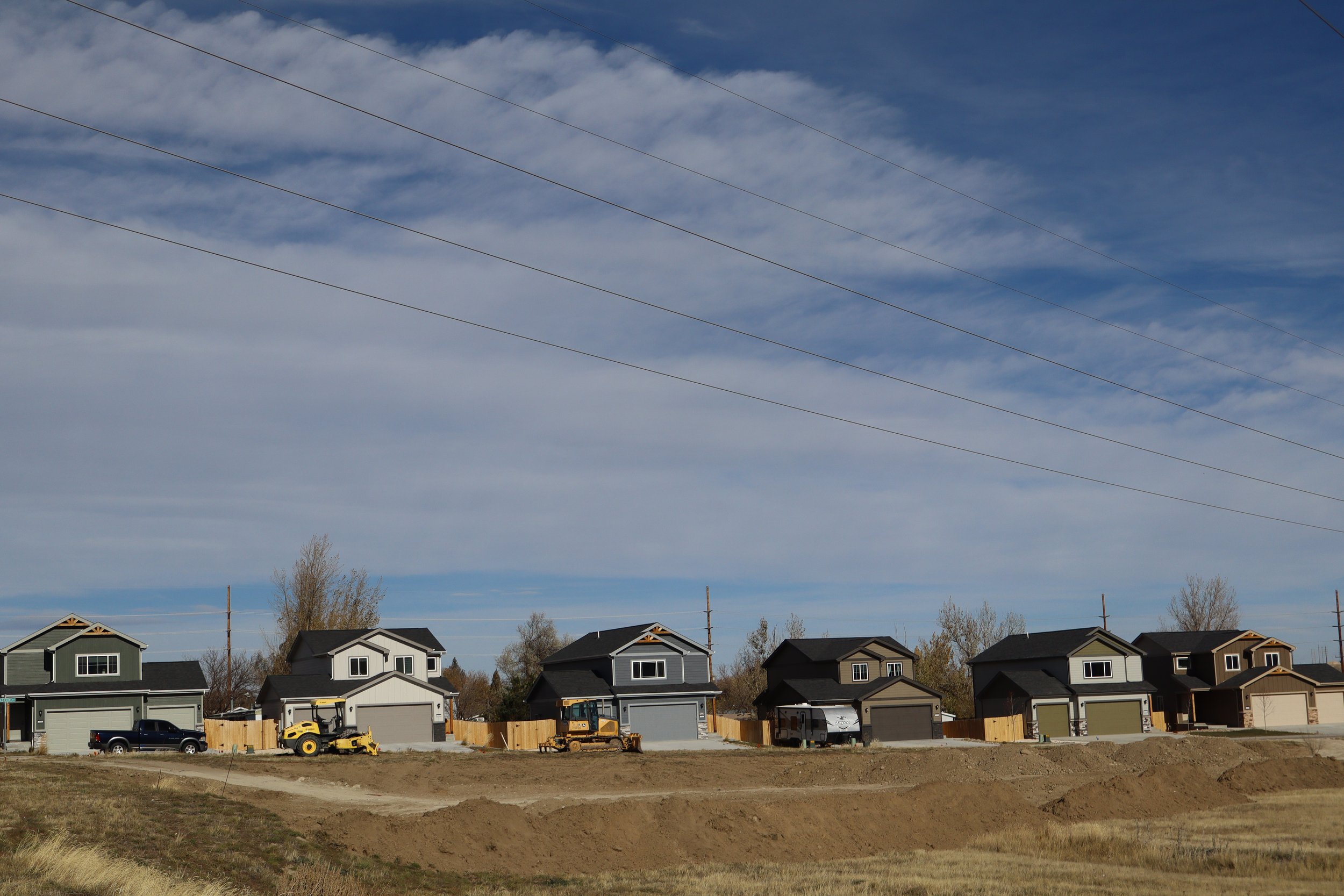 A row of newly built houses with trucks and construction equipment in front, under a partly cloudy sky.