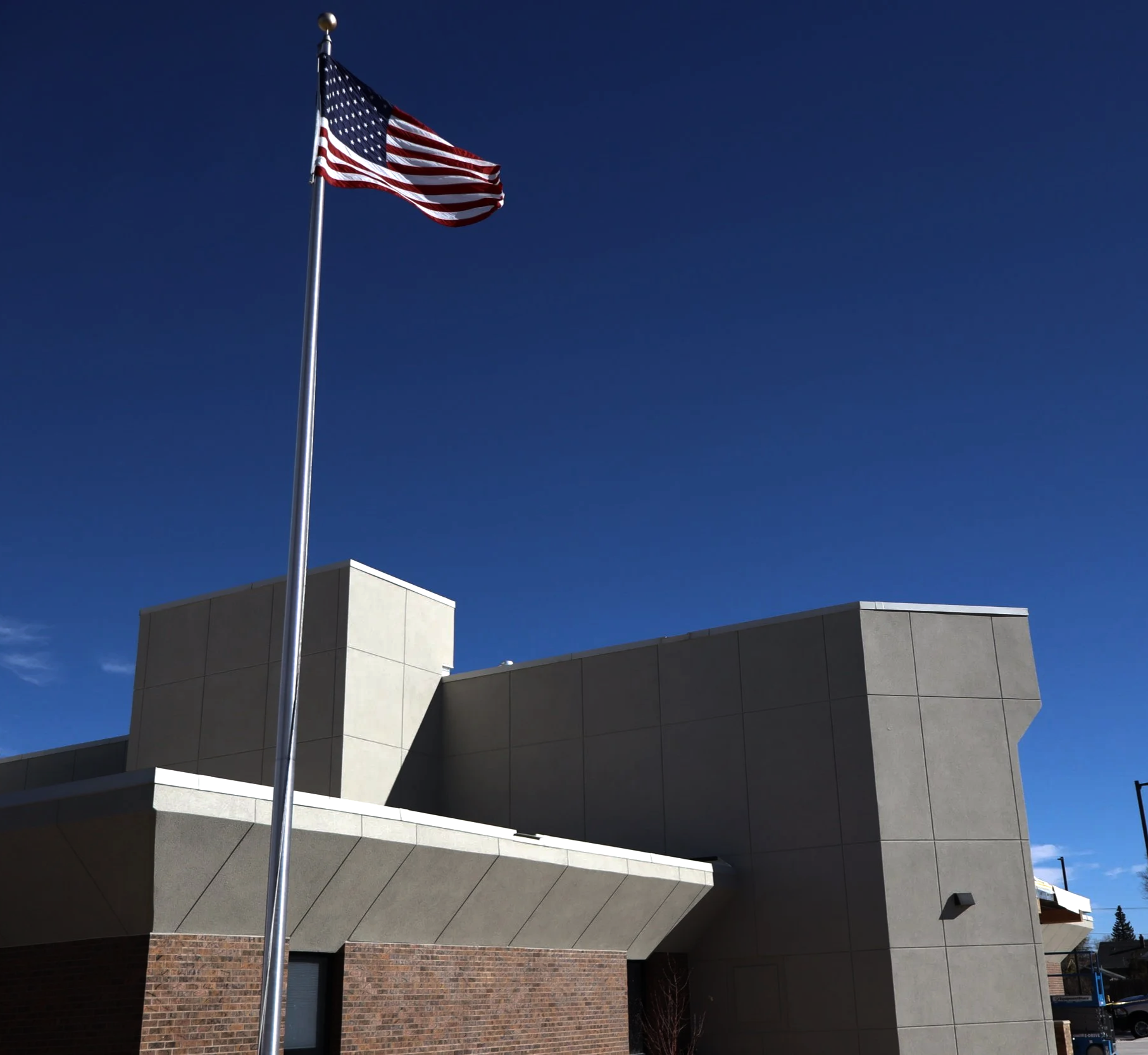 United States flag flying on a flagpole in front of a modern building with a blue sky background.