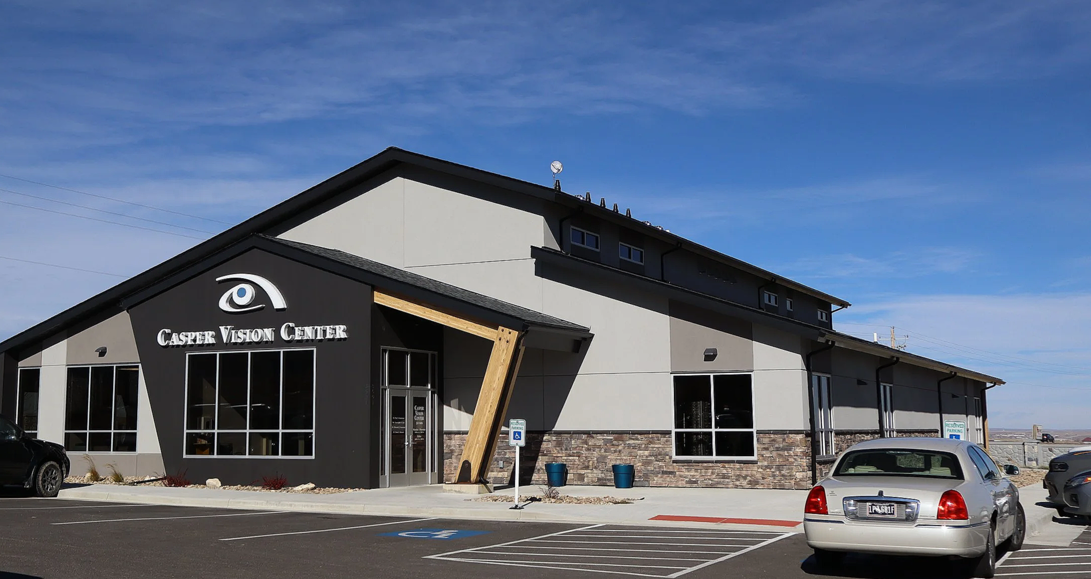 Exterior of the Casper Vision Center building with parking lot in front, cars parked, a handicap parking sign, and a clear blue sky.