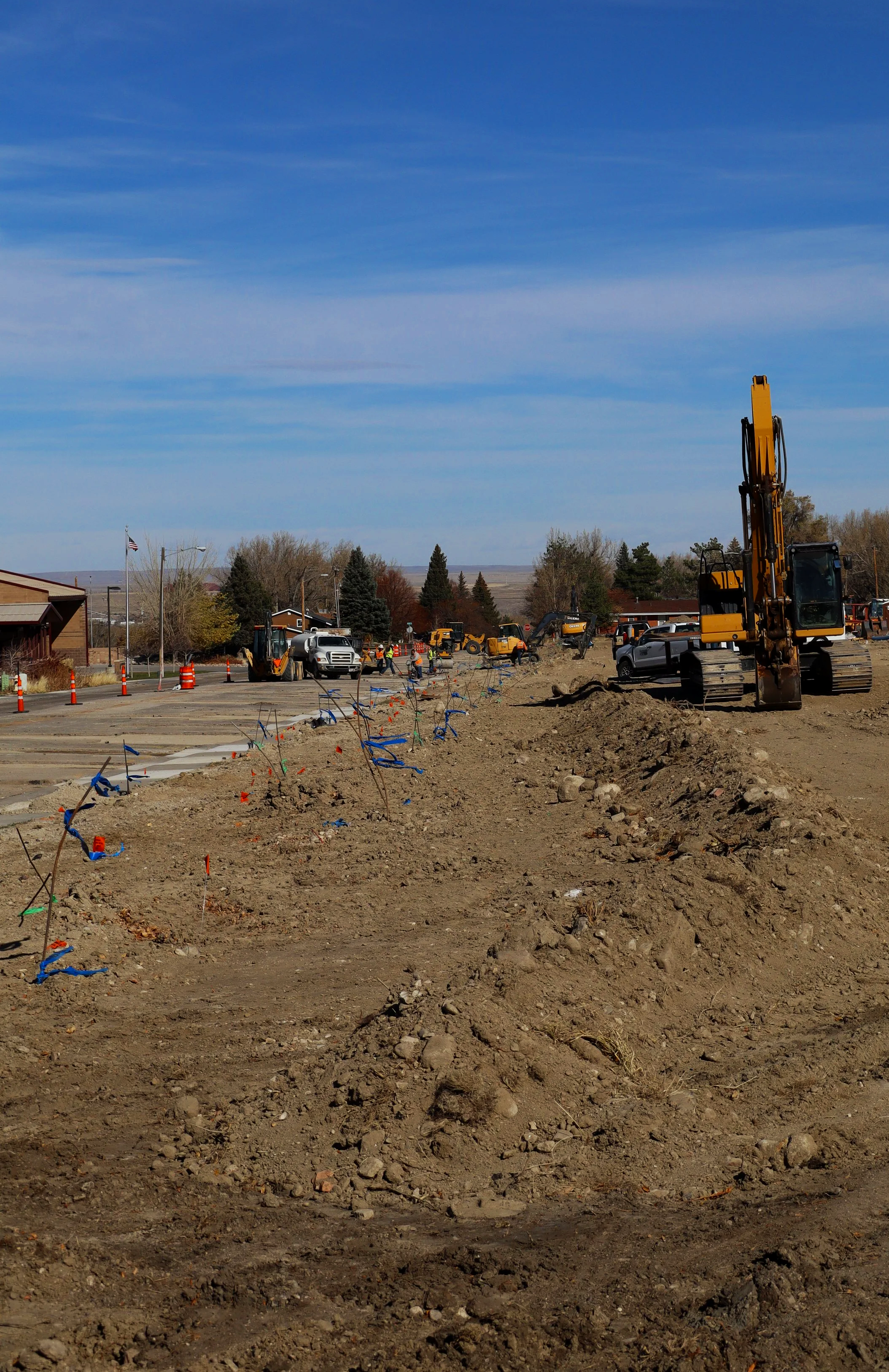 Construction site with heavy machinery, workers, and excavated dirt under a blue sky.