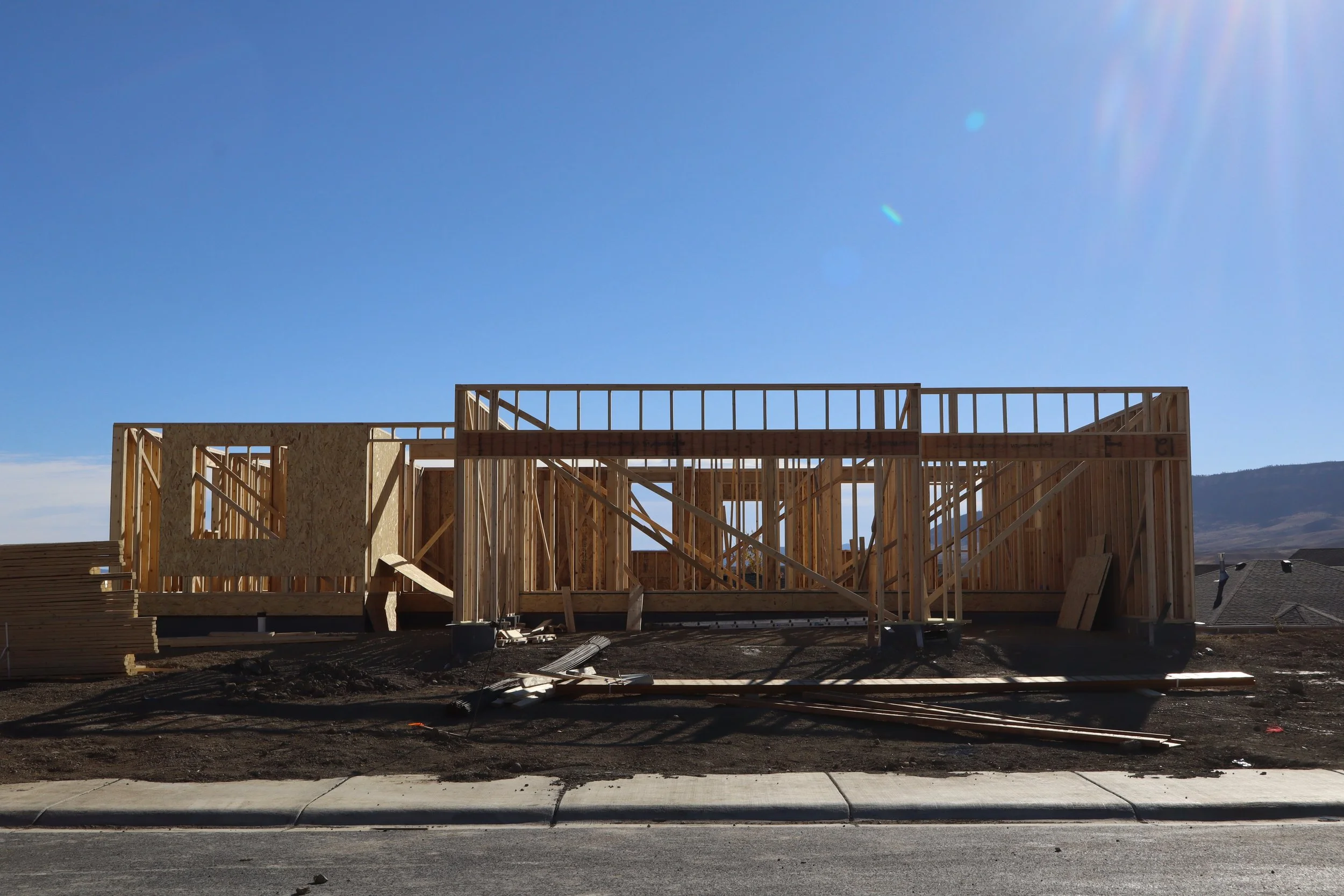 Framing of a new house under construction with wooden beams and structural supports on a construction site under a clear blue sky.