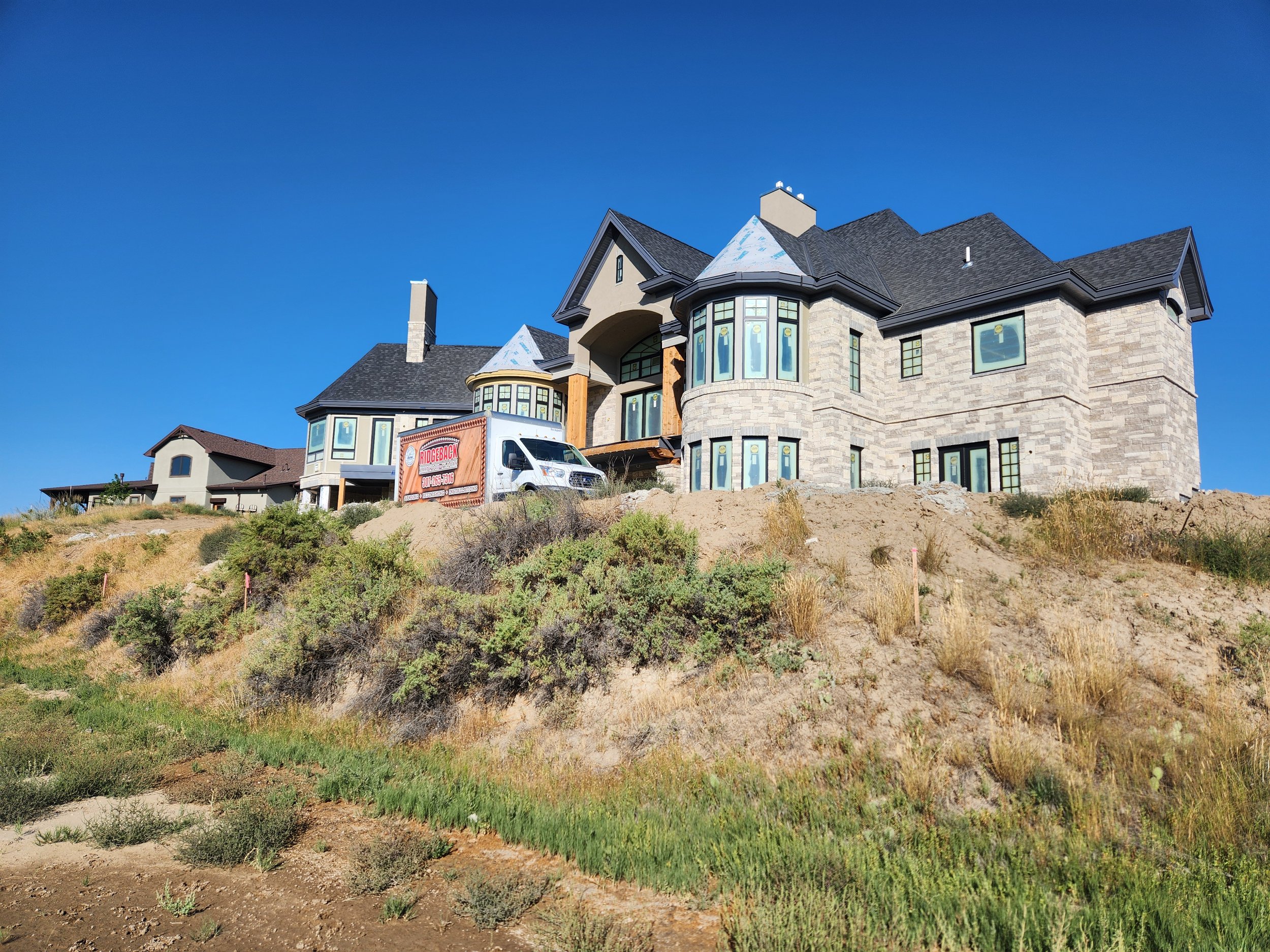 Large, modern house under construction on a hill with a clear blue sky.