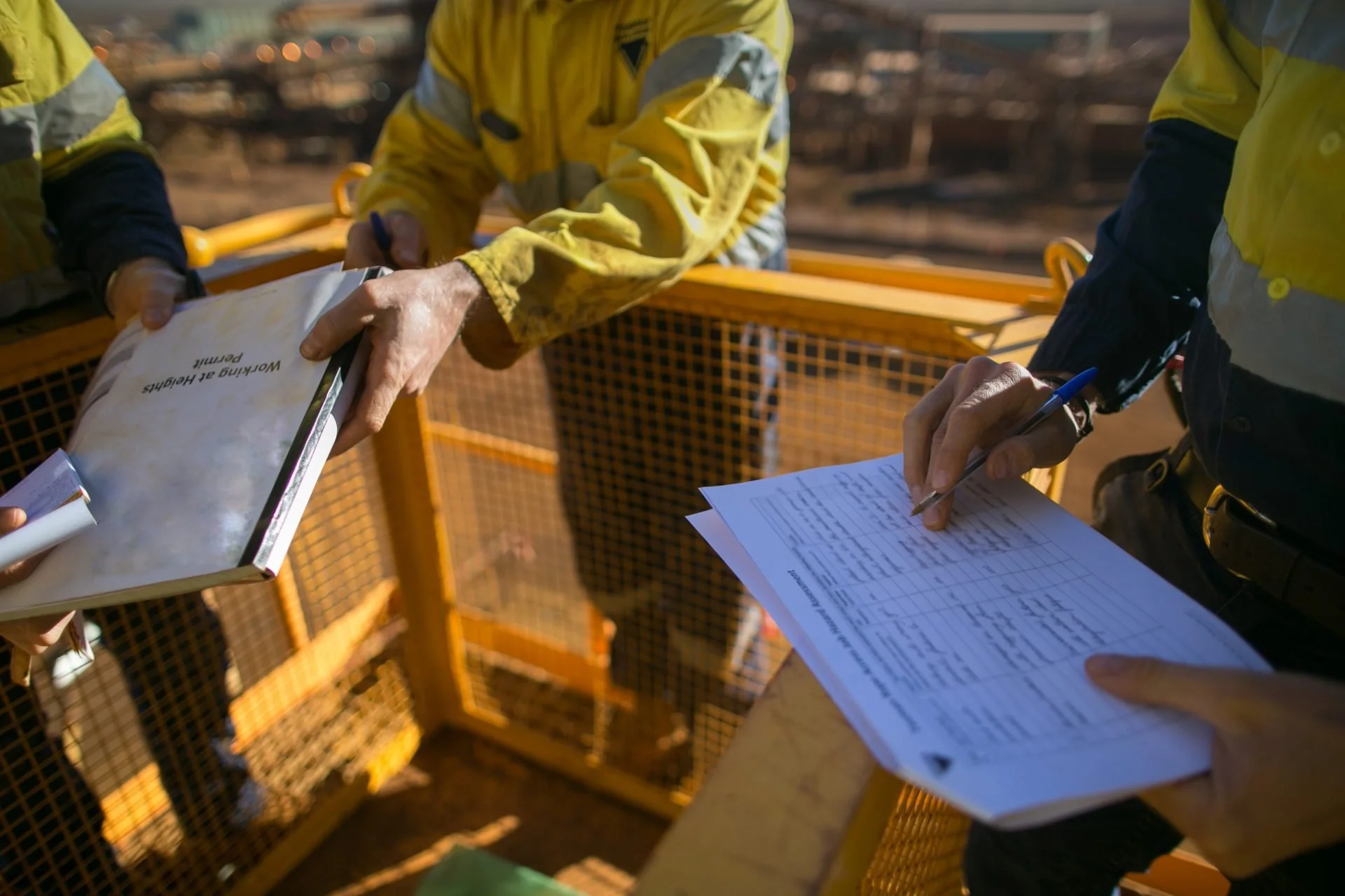 Workers in yellow safety gear at a construction site reviewing documents and charts.