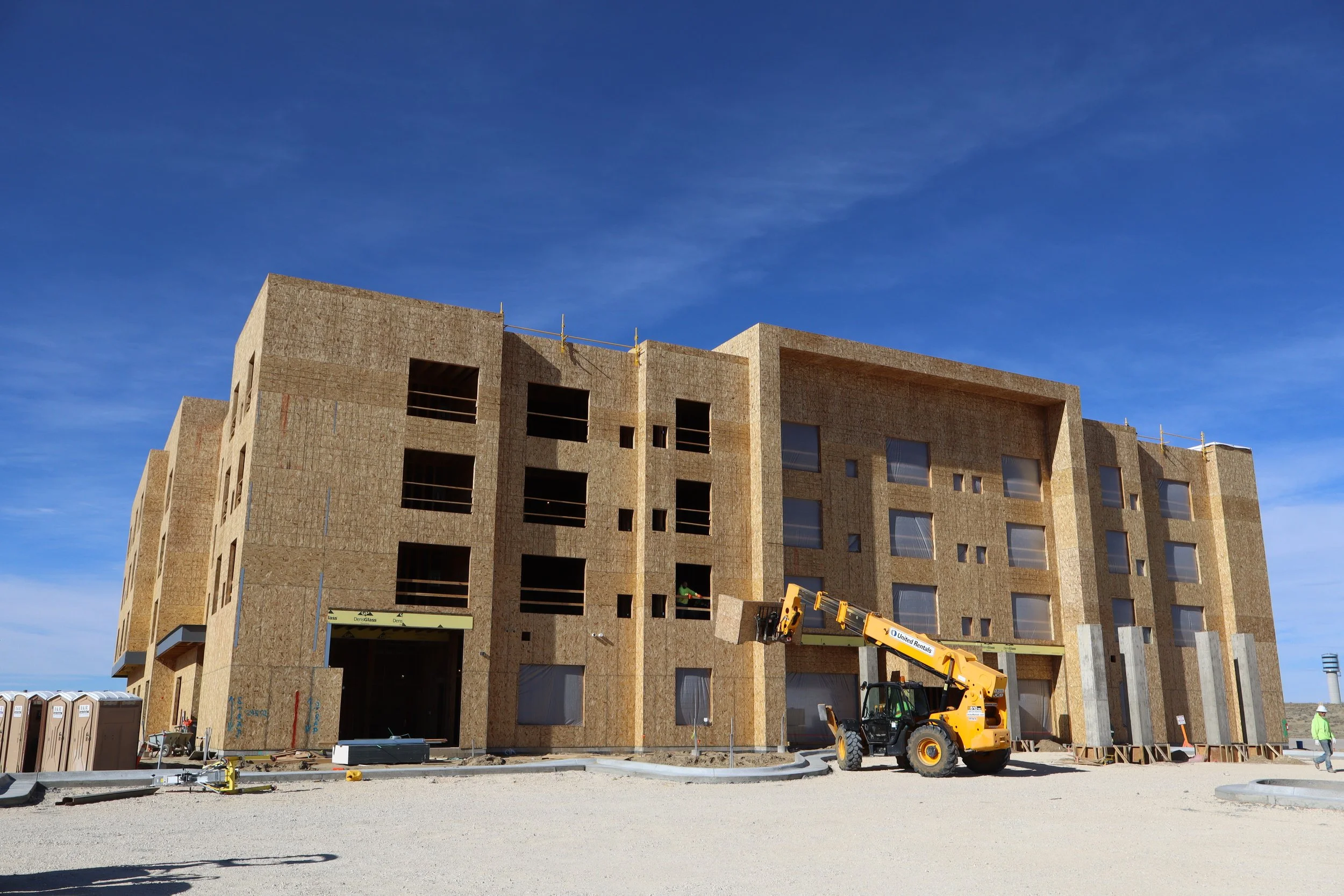 Construction site with a partially built multi-story building, a forklift, and workers under a clear blue sky.