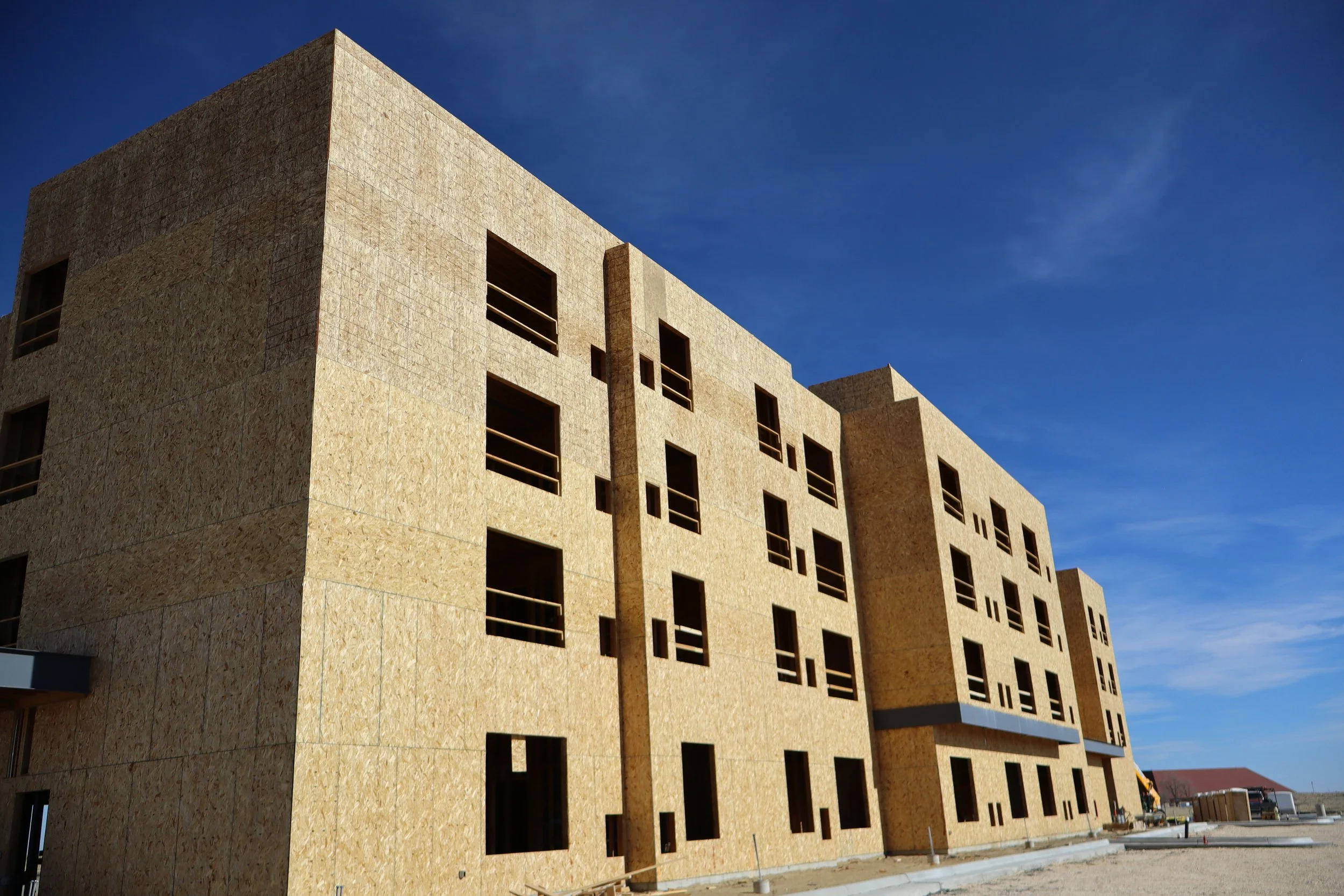 Under construction multi-story building with window openings, against a clear blue sky.