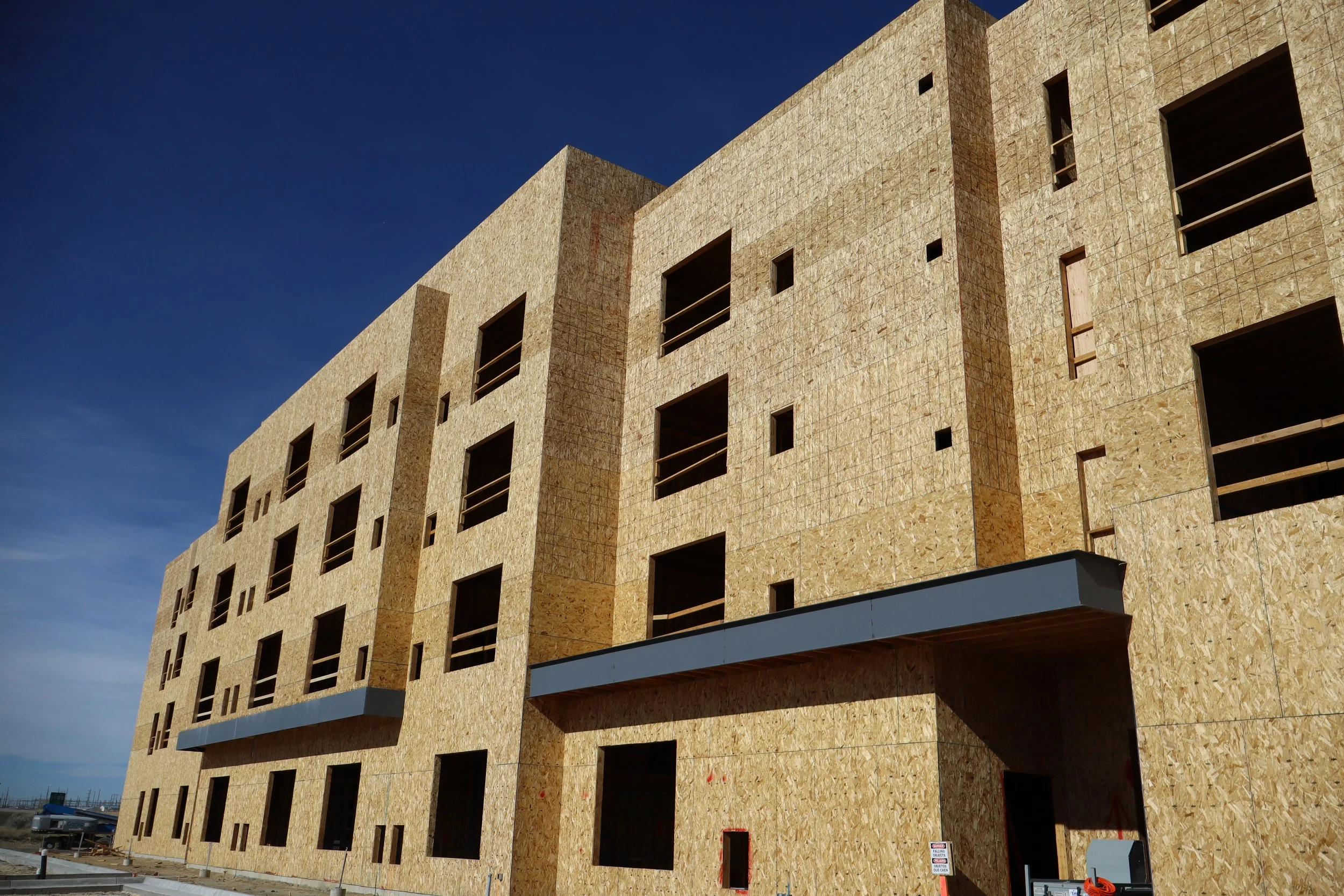 Under construction multi-story building with plywood exterior, several window openings, and a blue sky background.