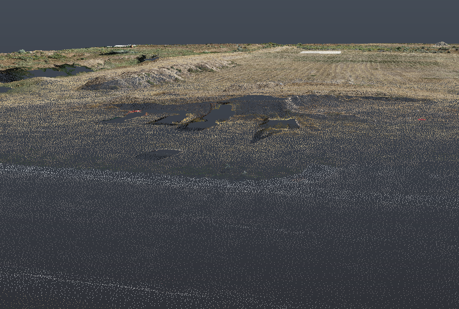 A flipped aerial view of an open field with patches of vegetation and small bodies of water, under a dark sky.