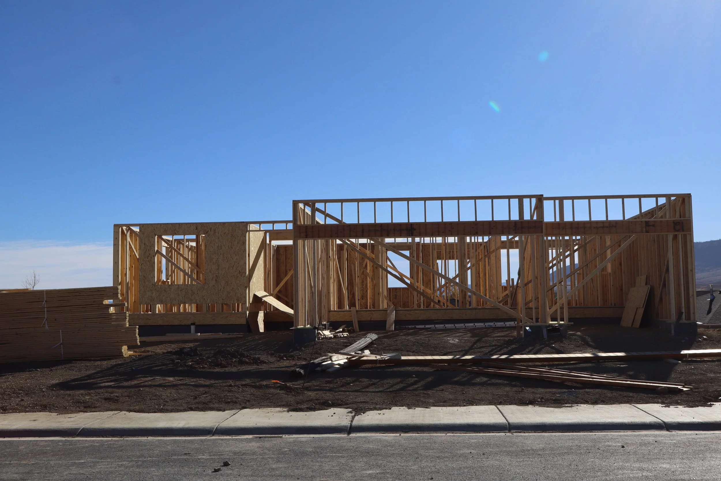 Wooden framing of a house under construction on a construction site, with a clear blue sky in the background.