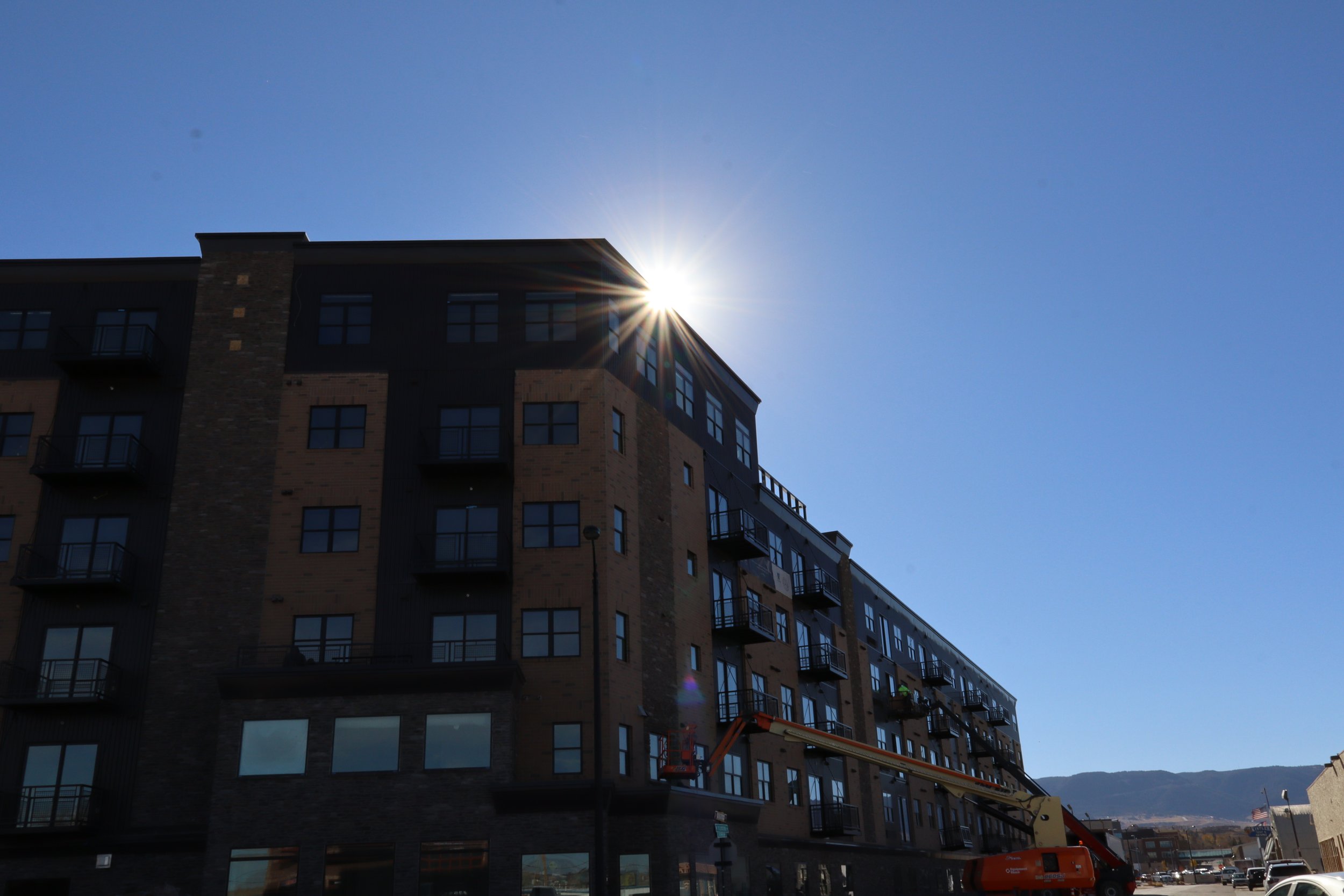 Modern multi-story apartment building with balconies, under construction or maintenance, with a lift and a worker in a yellow safety vest.