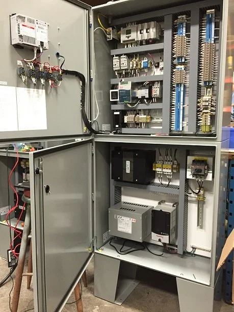 Electrical control panel with various components and wiring inside an open gray metal cabinet.