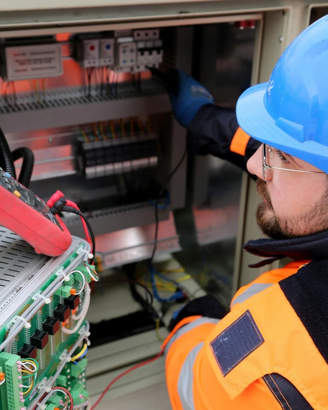 Worker in safety gear inspecting electrical components inside an electrical panel