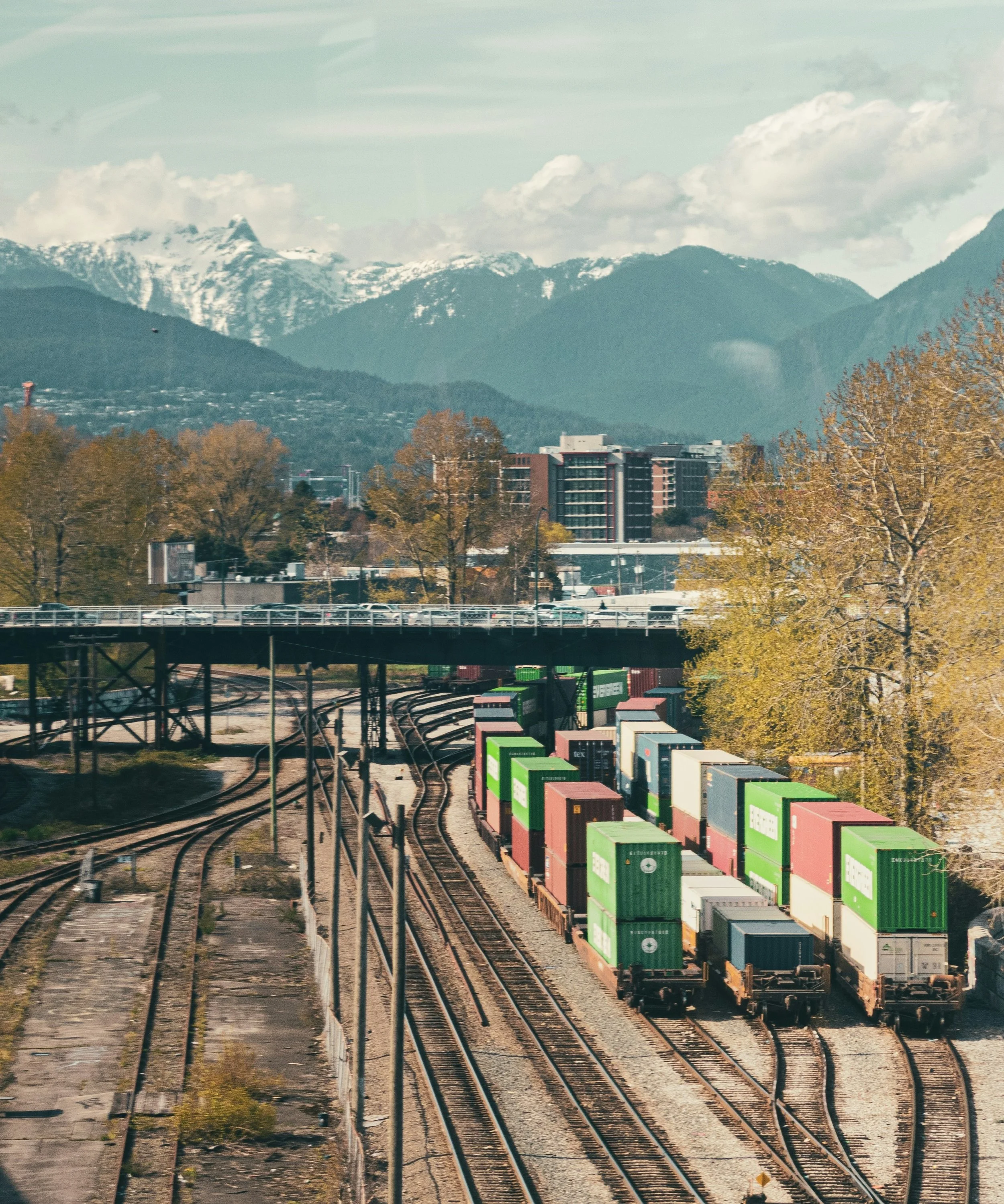 Cargo train carrying containers on a railway track with mountains and city buildings in the background.