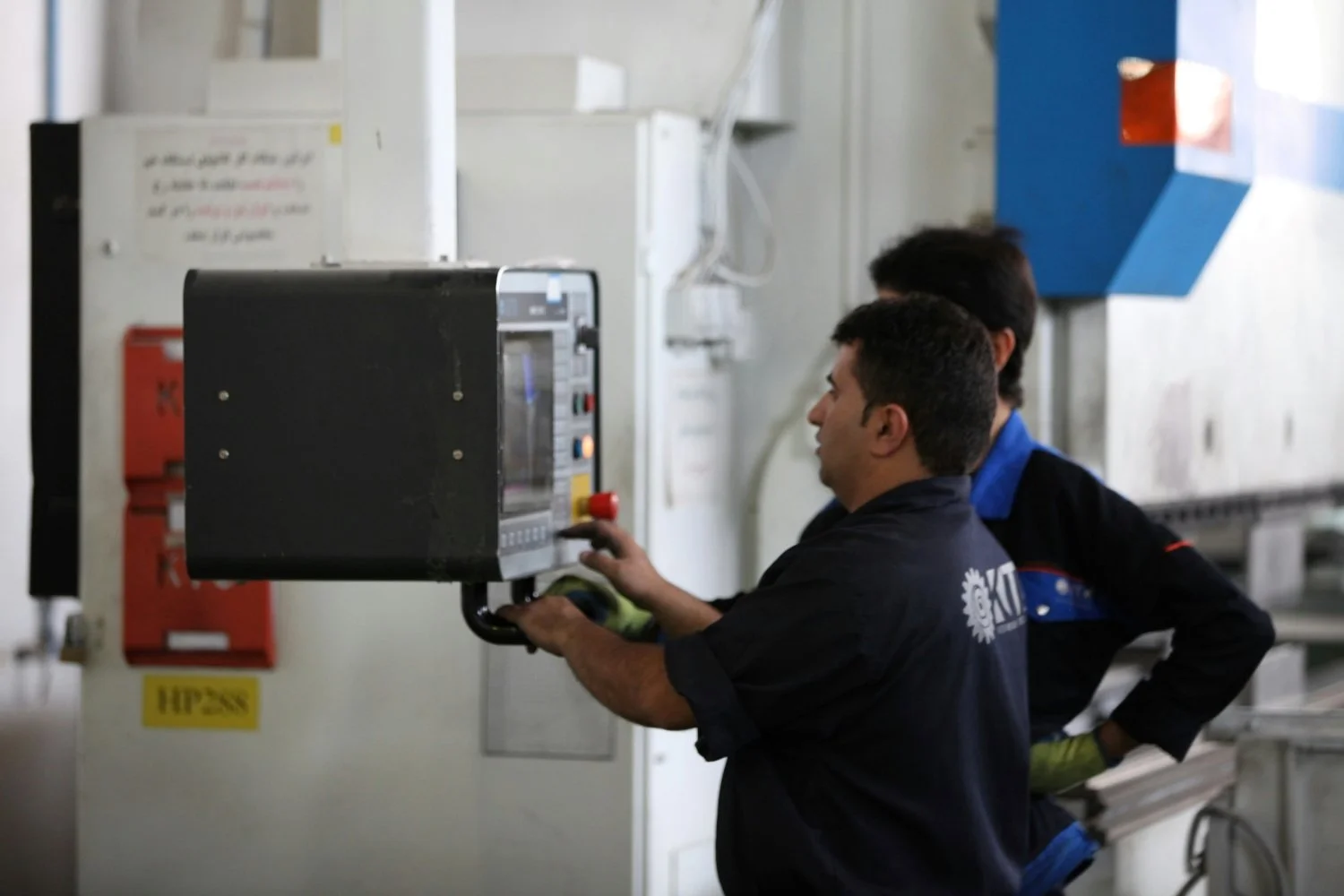 Two workers operating industrial machinery in a factory setting.