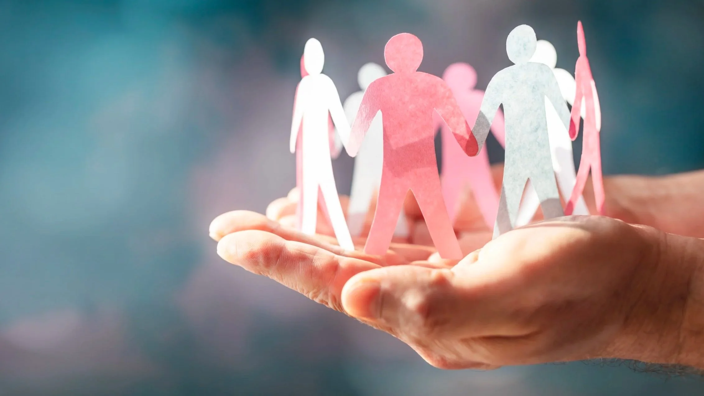 Hand holding a small paper-crafted representation of a diverse group of people holding hands.
