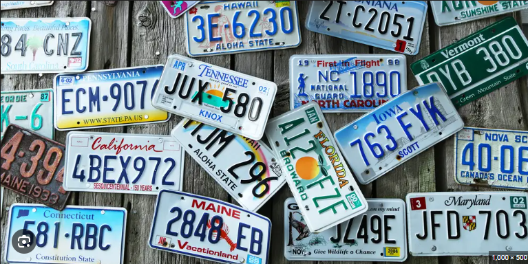 A collection of various license plates from different states, including Pennsylvania, California, Tennessee, Maine, Florida, Maryland, and others, arranged randomly on a wooden surface.