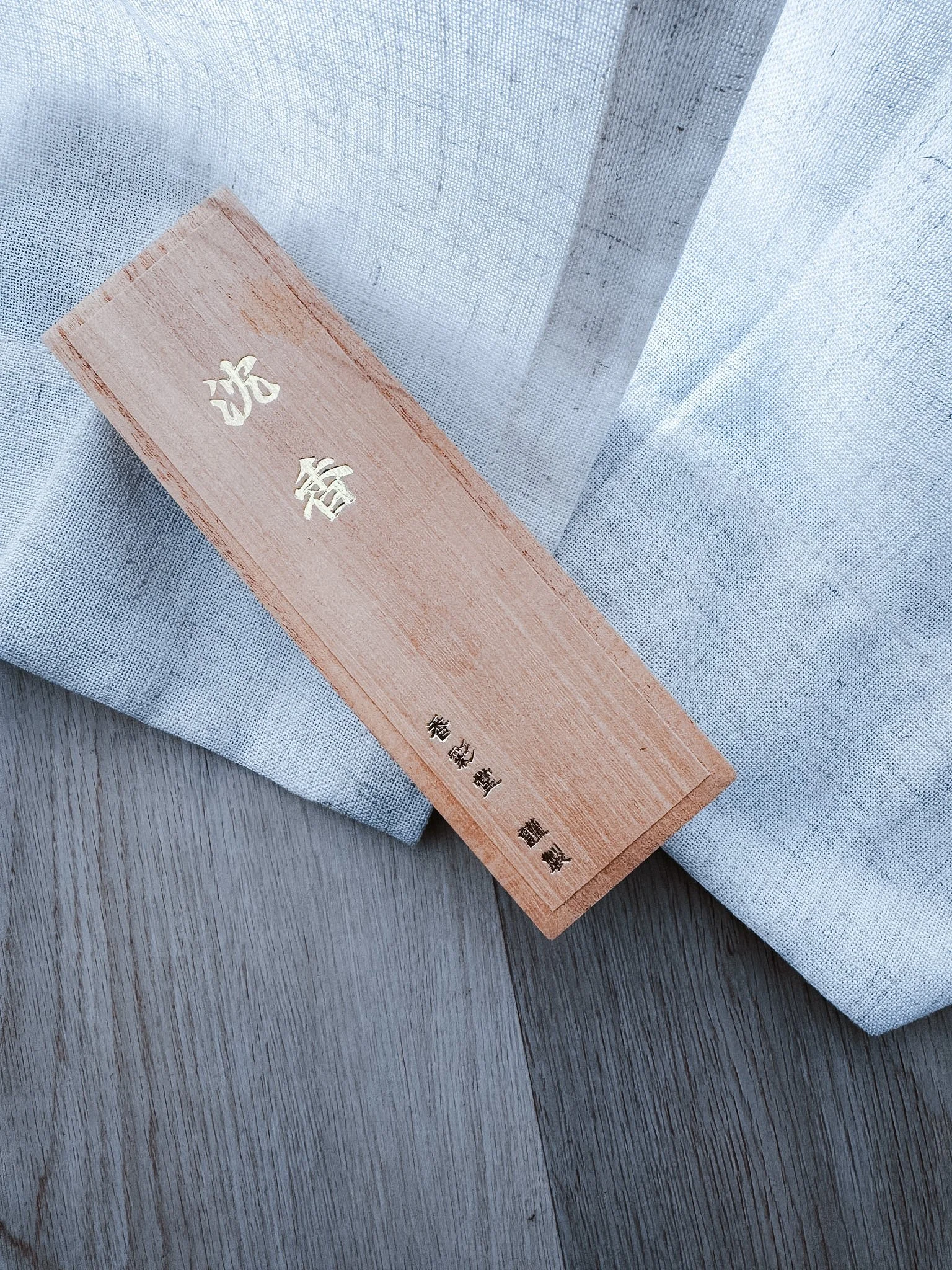 A wooden box with Japanese characters engraved on it, resting on a fabric surface.