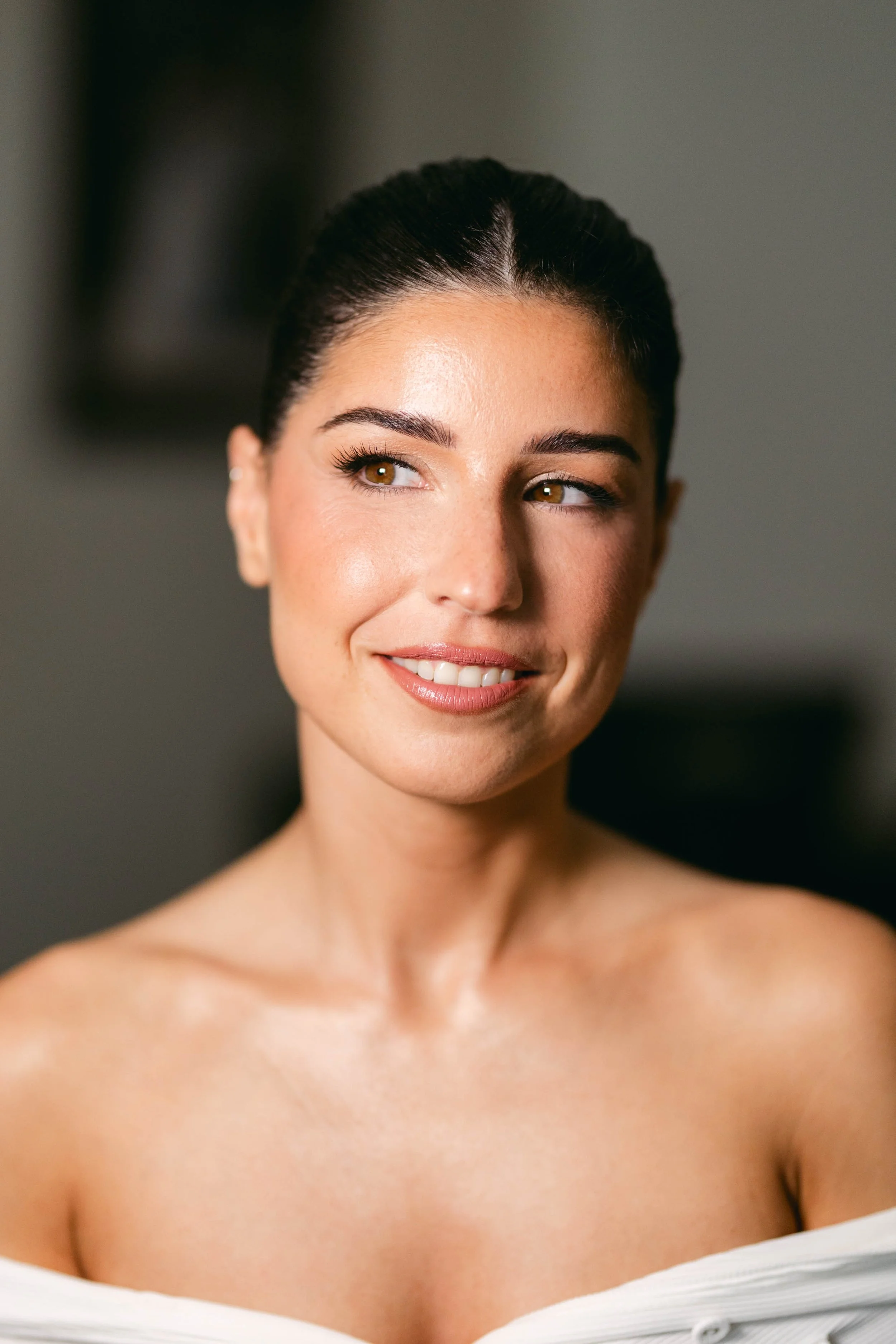 Close-up of a smiling woman with makeup and earrings, looking to the side, with dark hair pulled back.