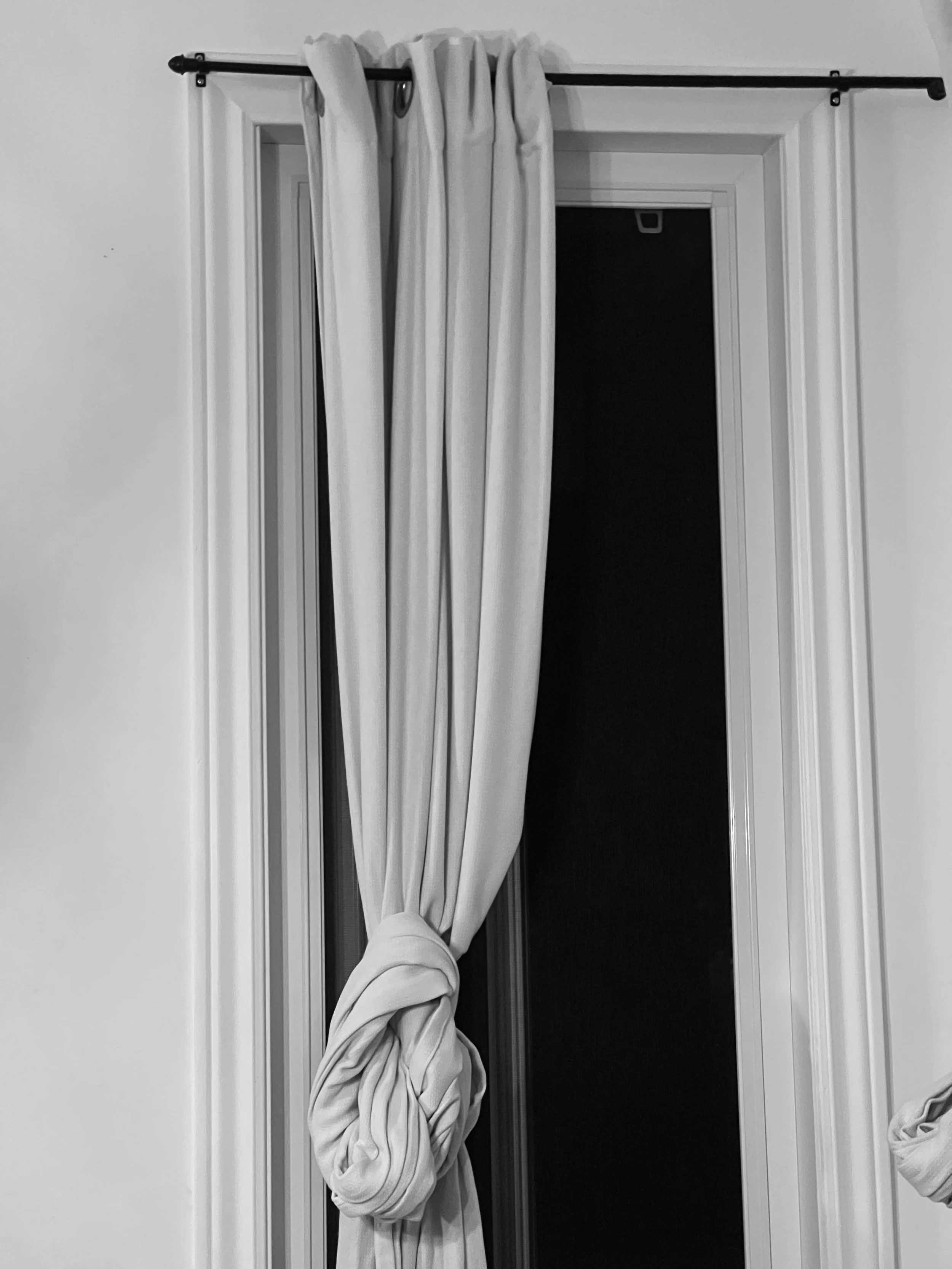 A curtain hanging on a curtain rod in front of a doorway, with the bottom of a person's leg visible.