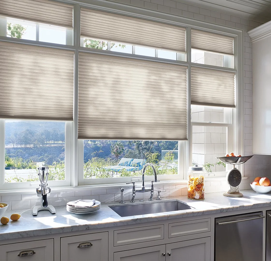 Kitchen with large window with blinds, marble countertop, sink, scale, fruit bowl, and jar of pasta, overlooking outdoor landscape.