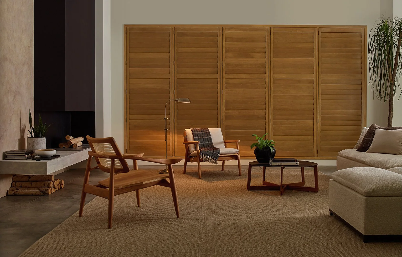 Living room with beige carpet, wooden chairs, a white sofa, a black vase with green plant, small coffee table, wood folding screen, and tall plant in corner.