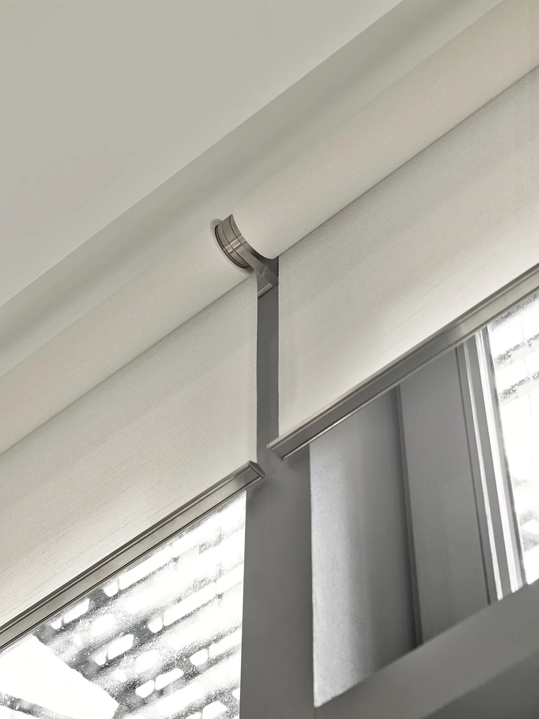 Close-up of a window with a Lutron white roller shade partially rolled up, showing a metal support rod.