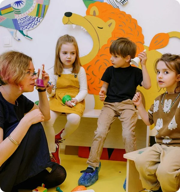 A woman and three children sitting on chairs in a colorful room with lion wall decor, engaging in a conversation or activity.