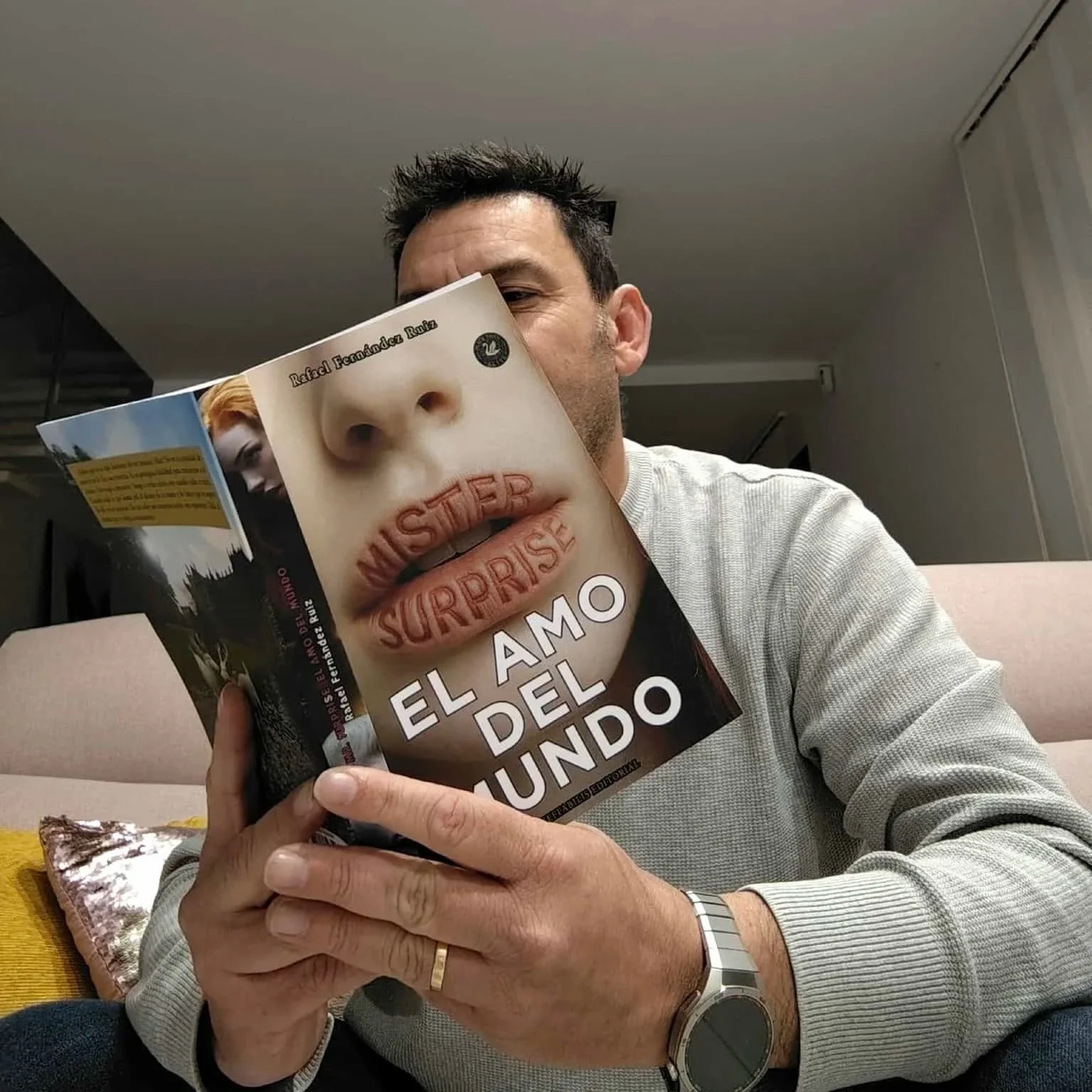 Una persona leyendo un libro en el sofá de su casa.