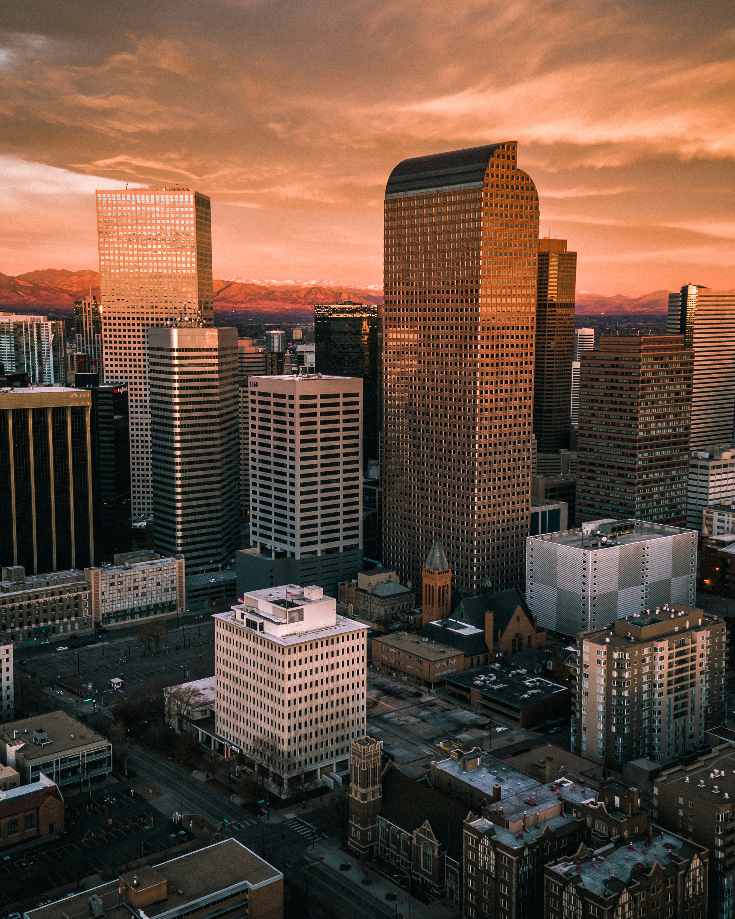Sunset over a city skyline with tall skyscrapers and mountain range in the background.