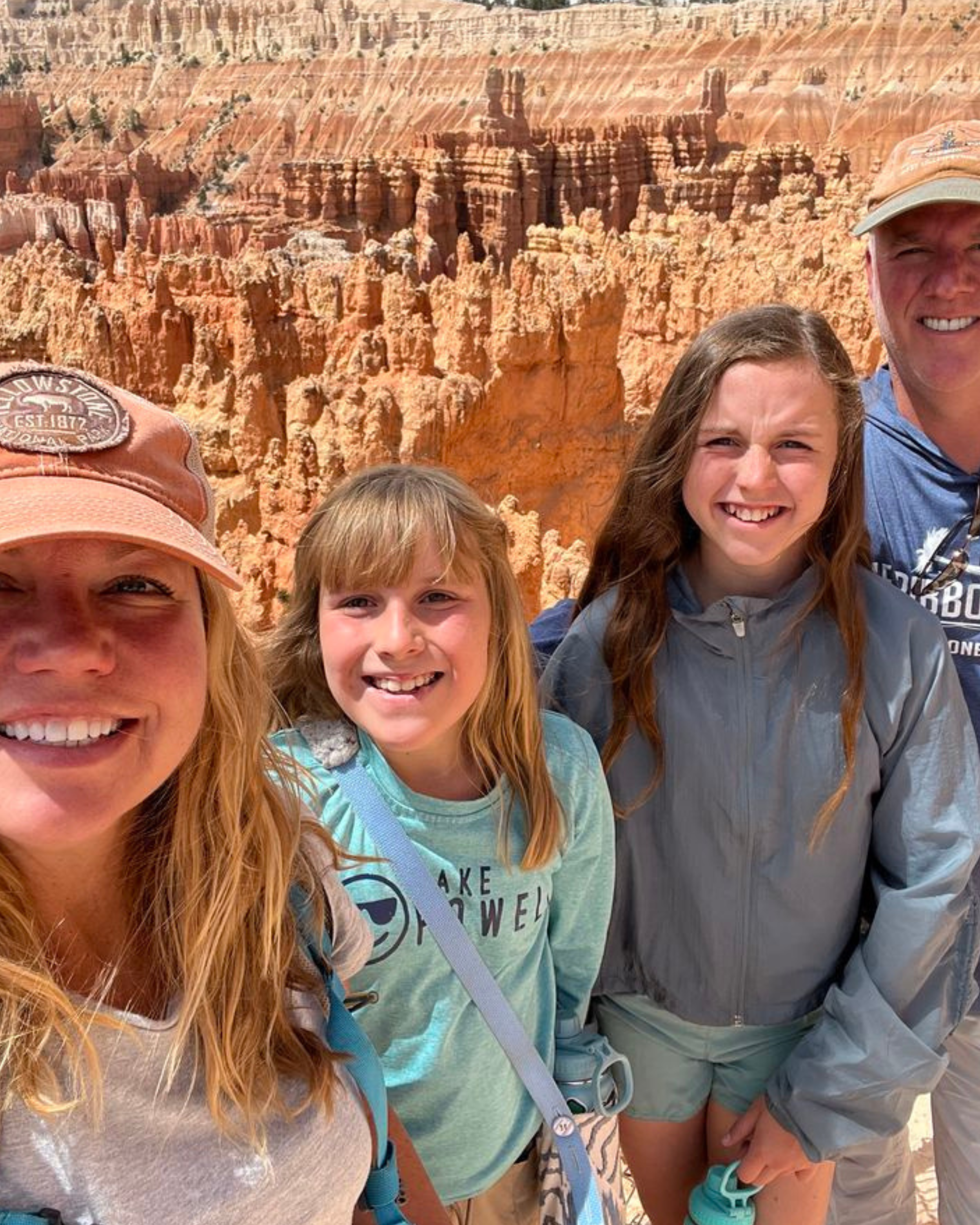 A group of four people taking a selfie in front of the orange rock formations of the Grand Canyon.