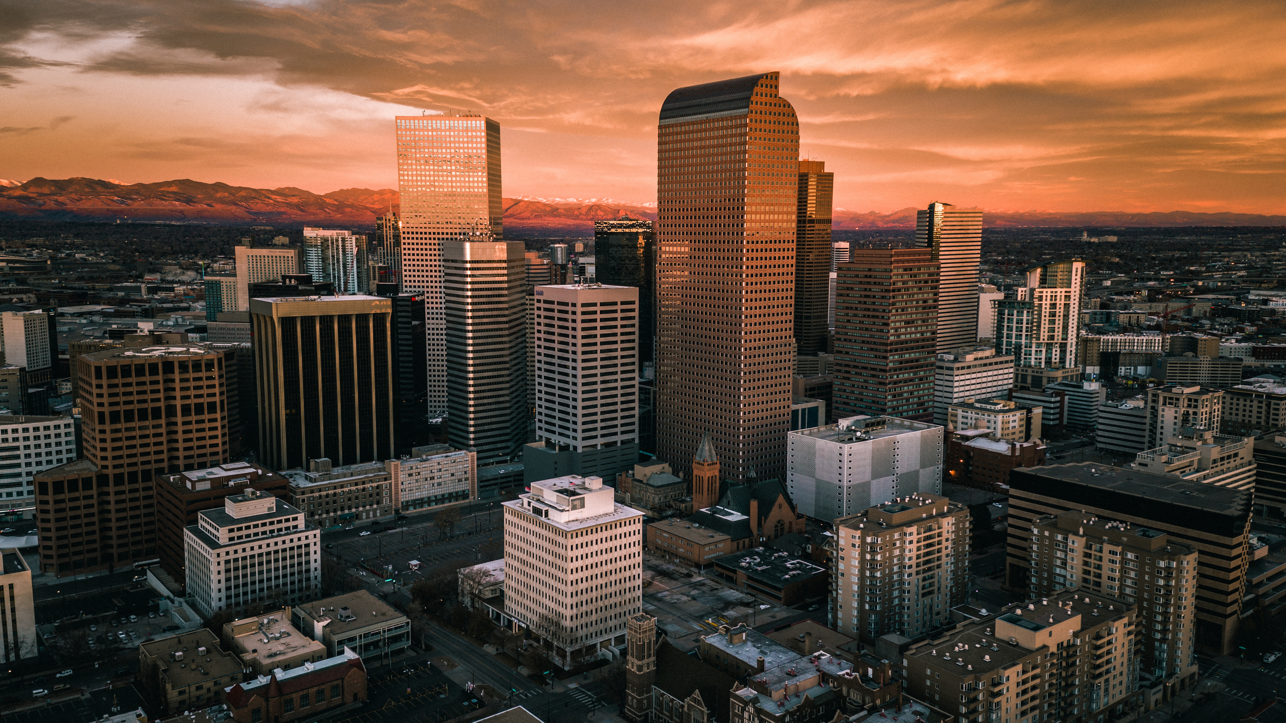City skyline at sunset with tall buildings and mountains in the background.