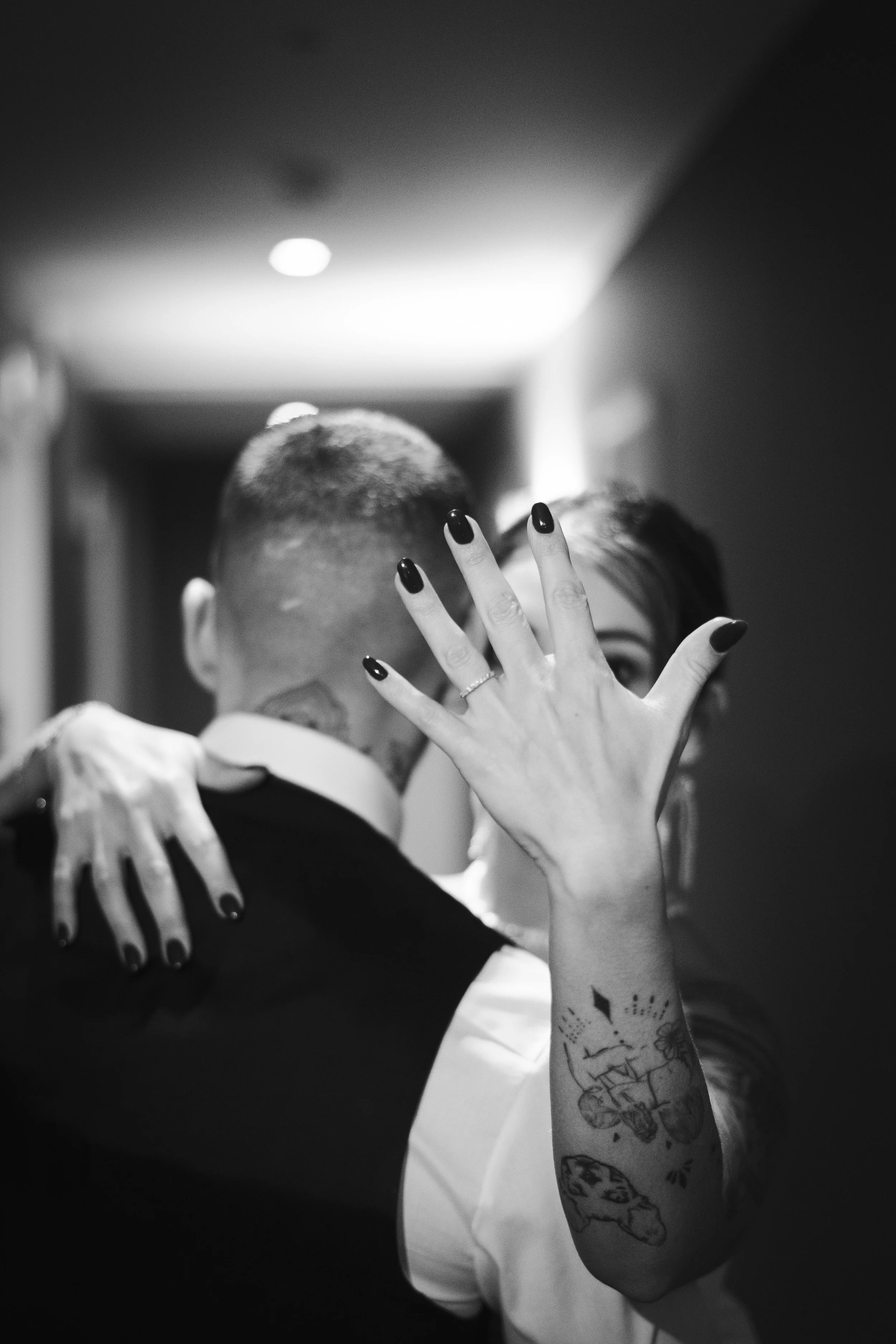 Un couple qui danse et s'embrasse dans un couloir, en noir et blanc, avec une femme qui tient la main de l'homme et montre ses tatouages.
