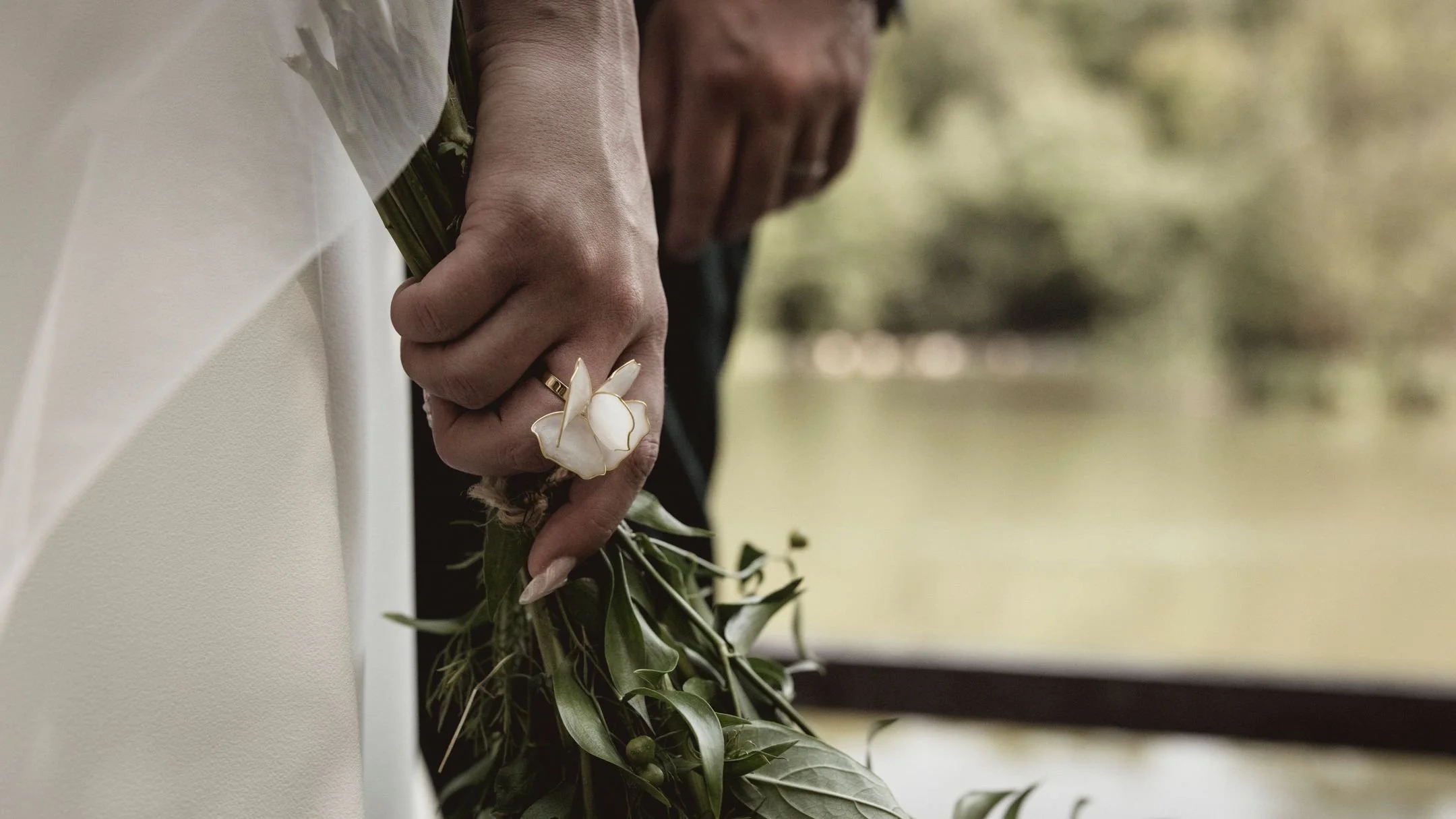 Gros plan sur une main tenant un bouquet de fleurs avec une bague en forme de fleur blanche.