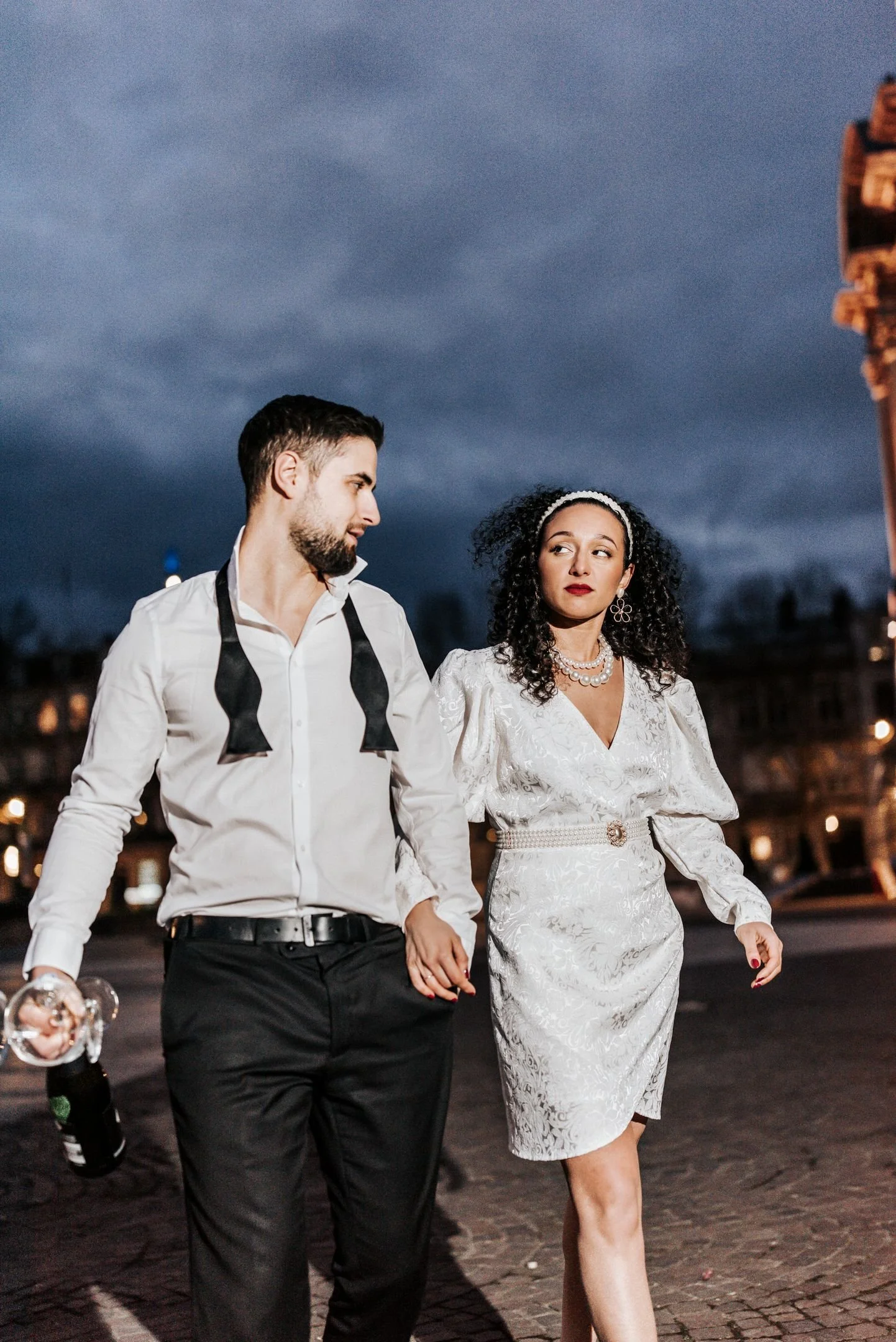 Un couple marchant main dans la main à Paris, la nuit, avec la Tour Eiffel en arrière-plan.