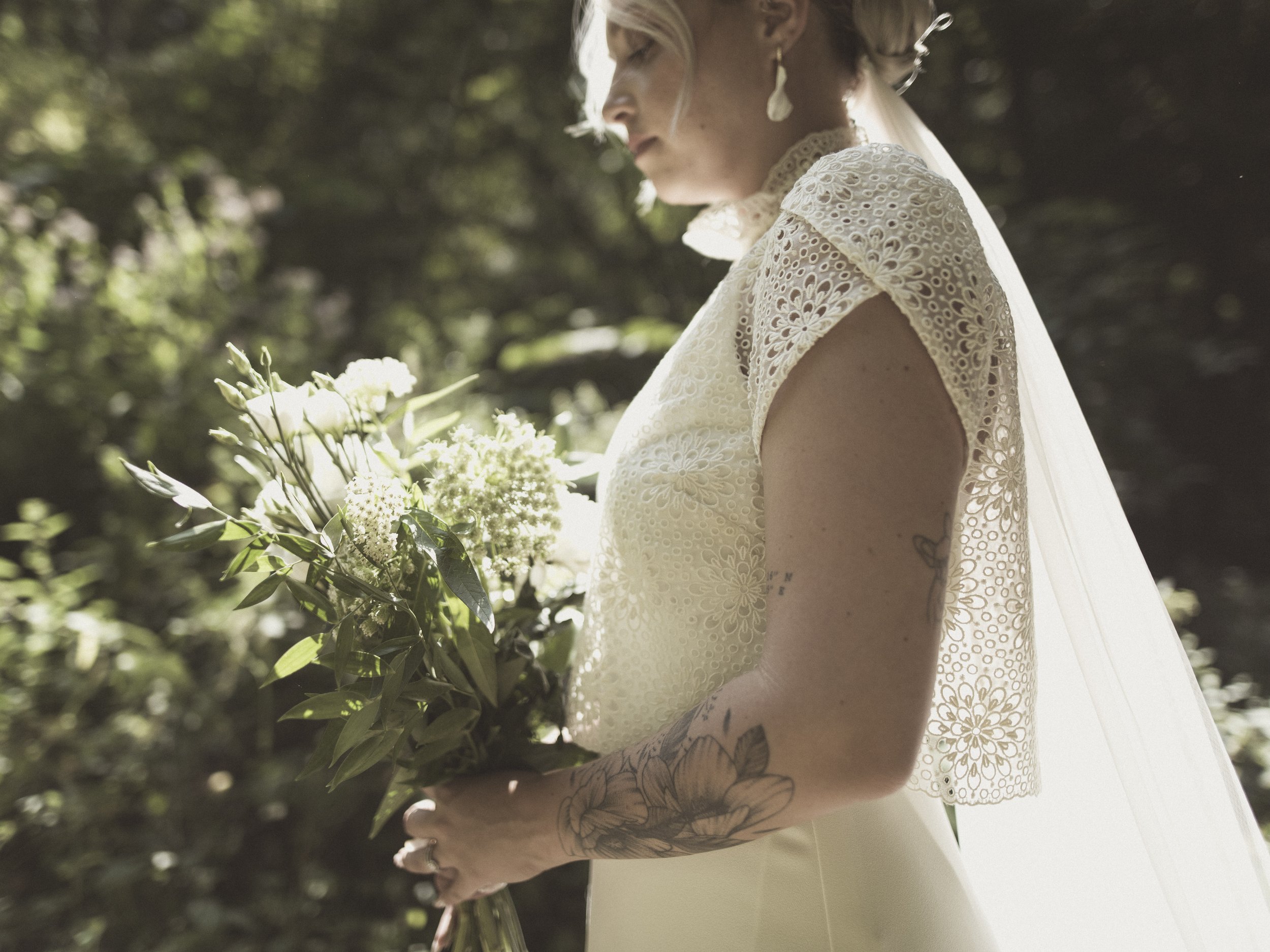 Une femme en robe de mariée tient un bouquet de fleurs, se tenant à l'extérieur dans un environnement verdoyant.