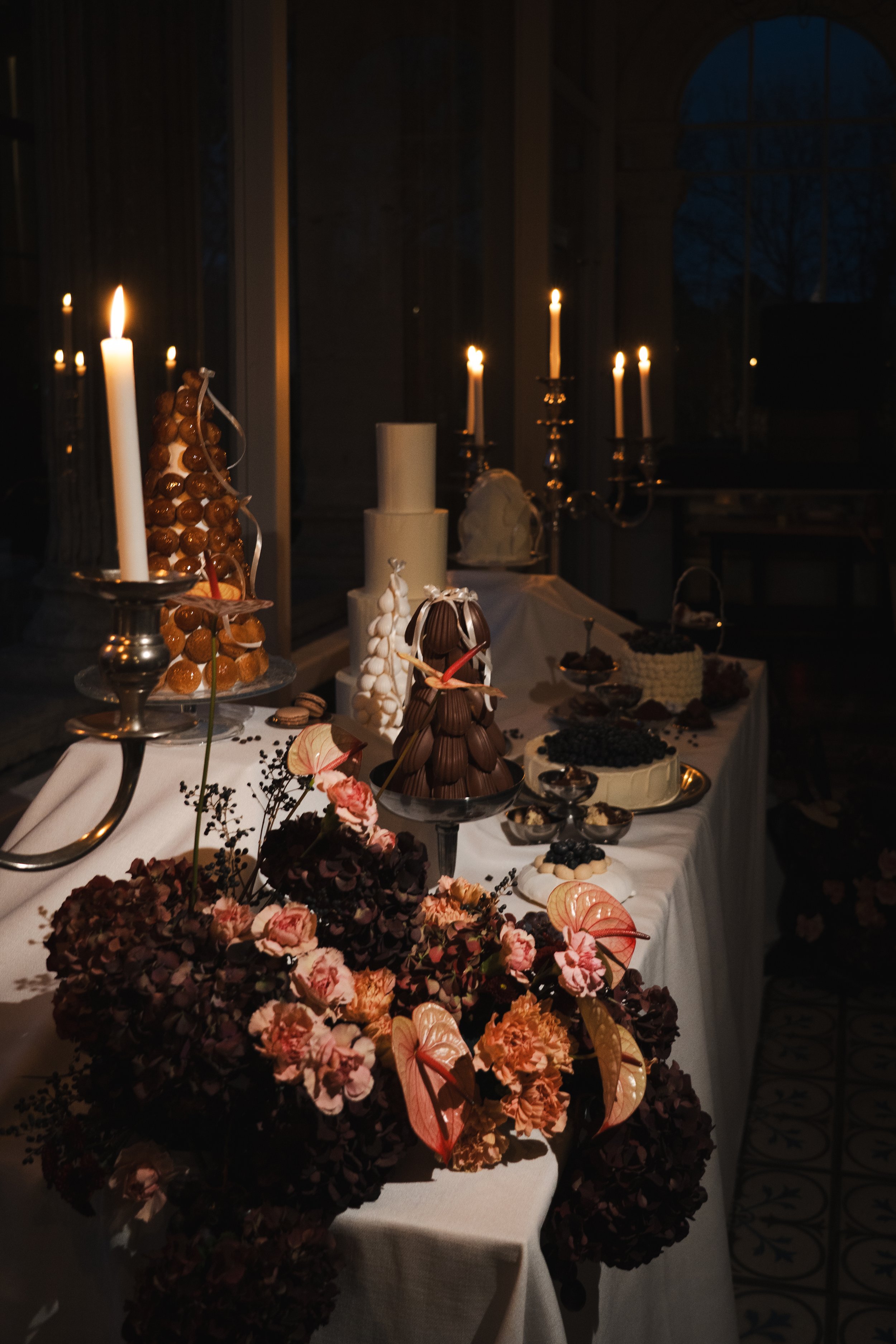 Table de desserts décorée avec des fleurs, des chandelles allumées et des gâteaux dans un environnement sombre et élégant.