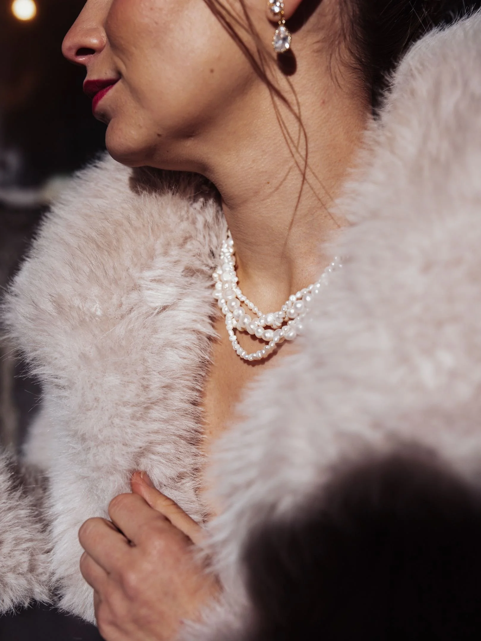 Une femme élégante portant des bijoux en perles, une robe ou manteau en fourrure beige, avec des détails en bijoux et maquillage rouge.