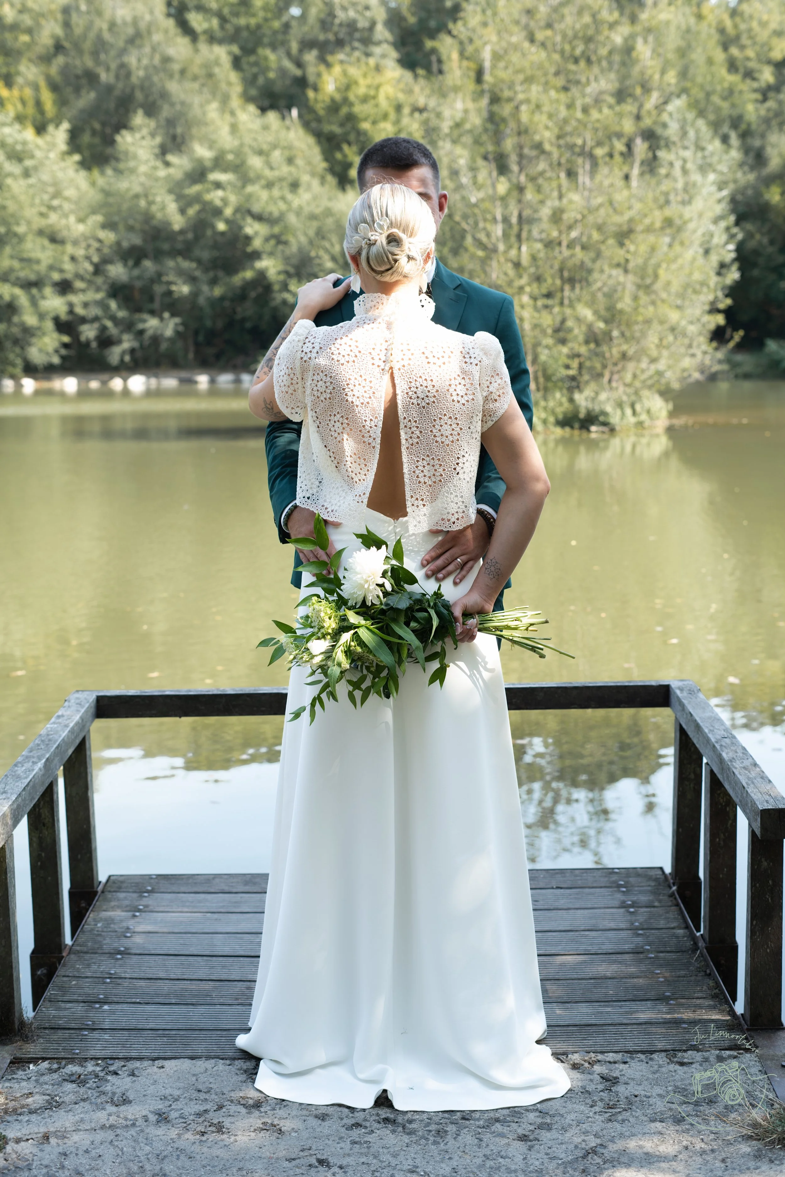 Un couple de mariés s'embrassant au bord d'un lac entouré d'arbres verts.