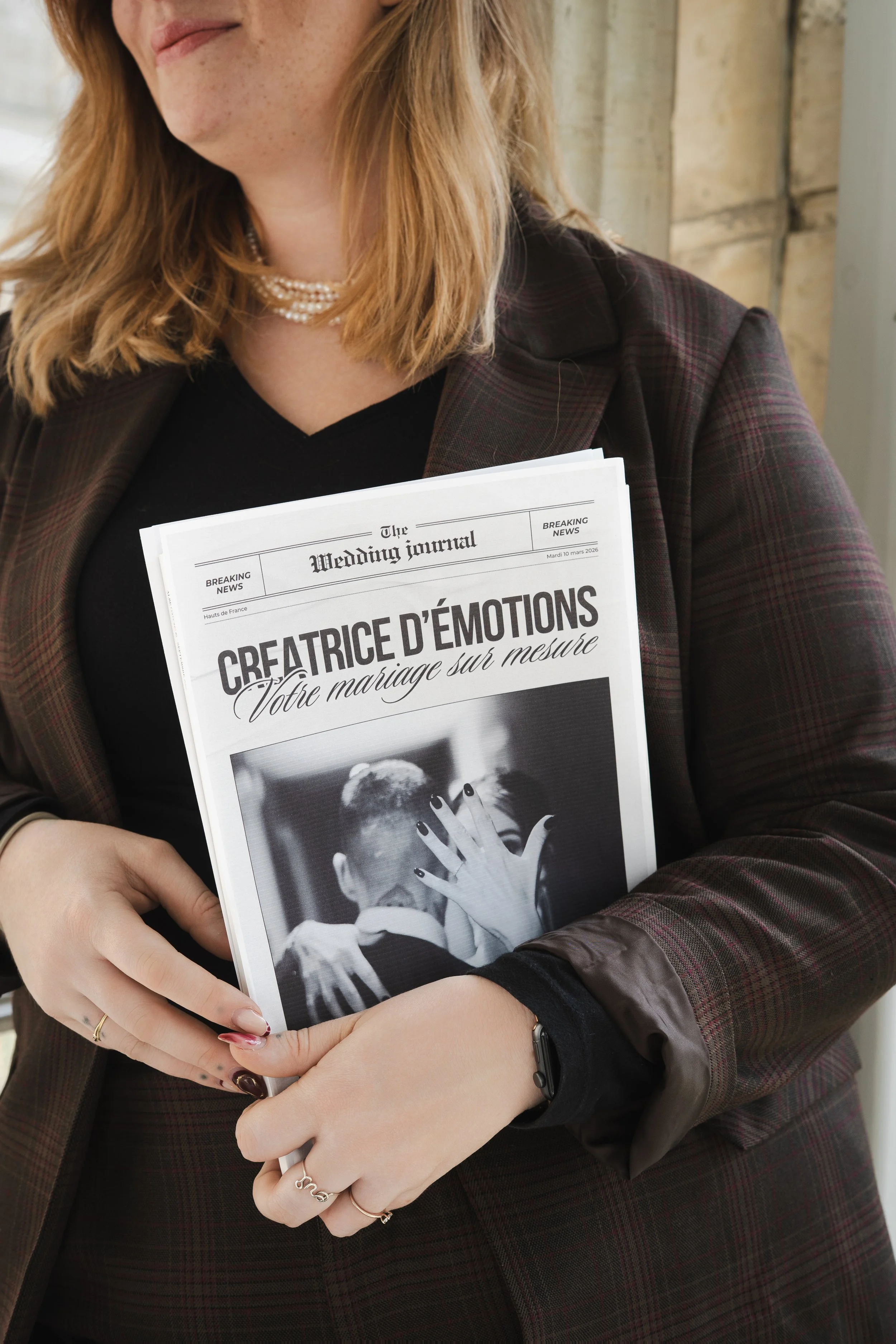 Une femme tenant un journal intitulé 'The Wedding Journal' avec une photo en noir et blanc d'une personne masquée, drapée de noir, avec les mains levées.