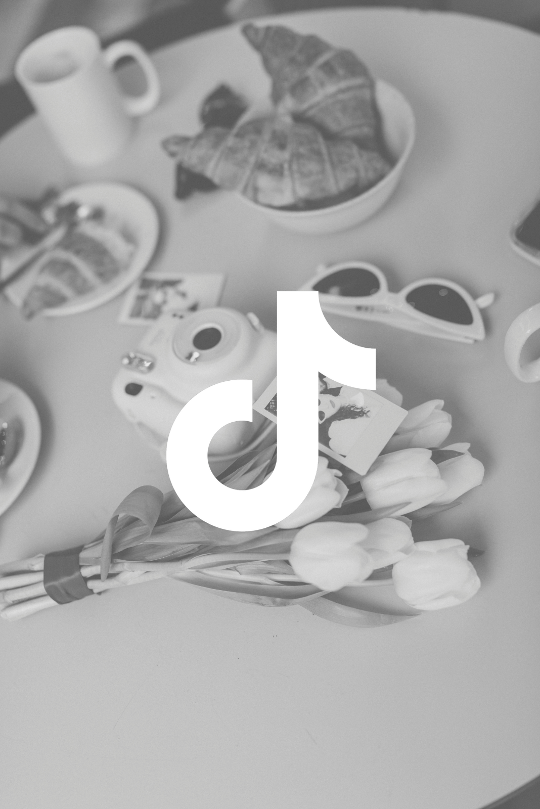 Une table avec des croissants, des tasses, des lunettes de soleil, une bouquet de tulipes, une caméra instantanée, et des photographies.