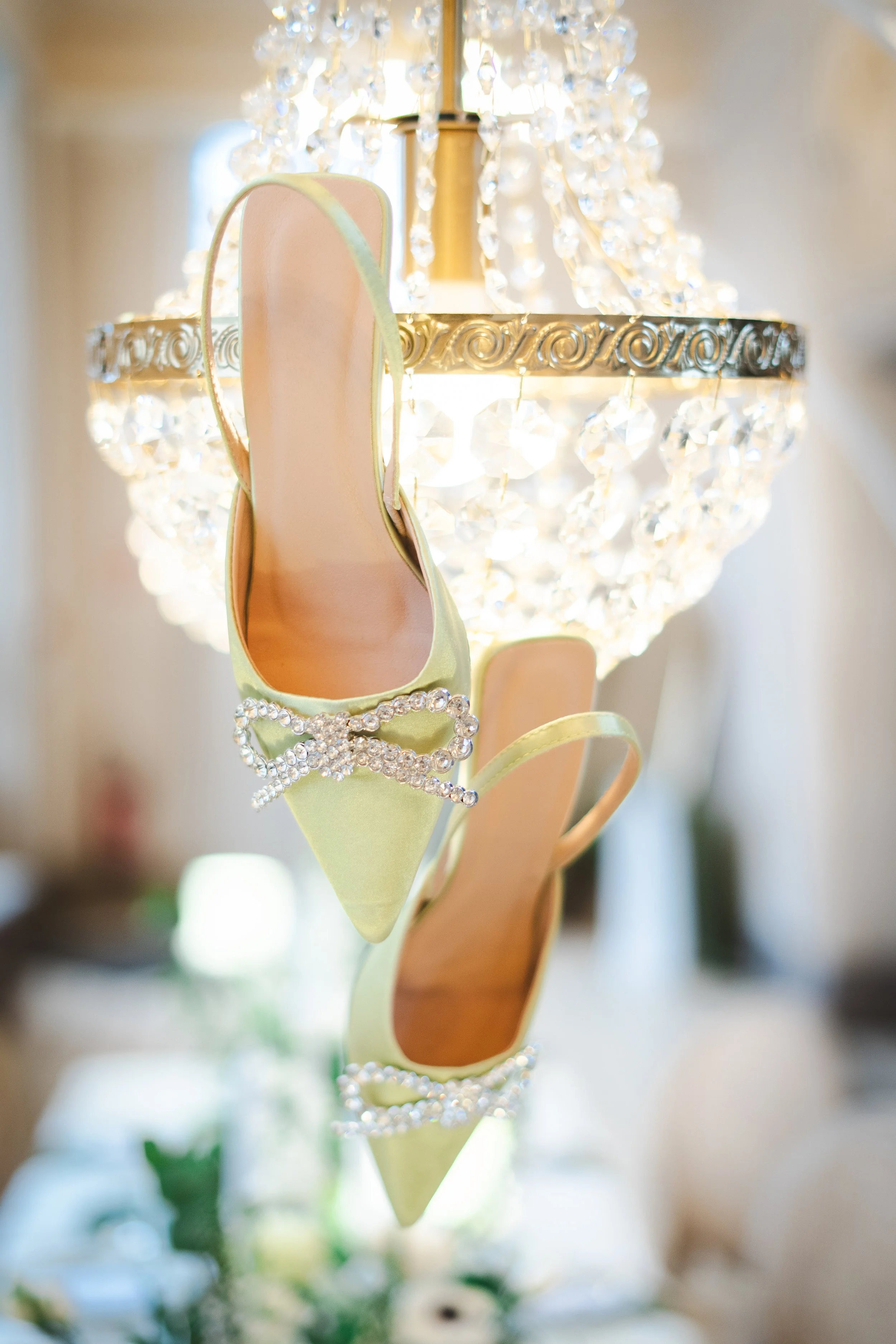 Une paire de chaussures de cérémonie lime avec des détails en perles, suspendues sous un chandelier en cristal.