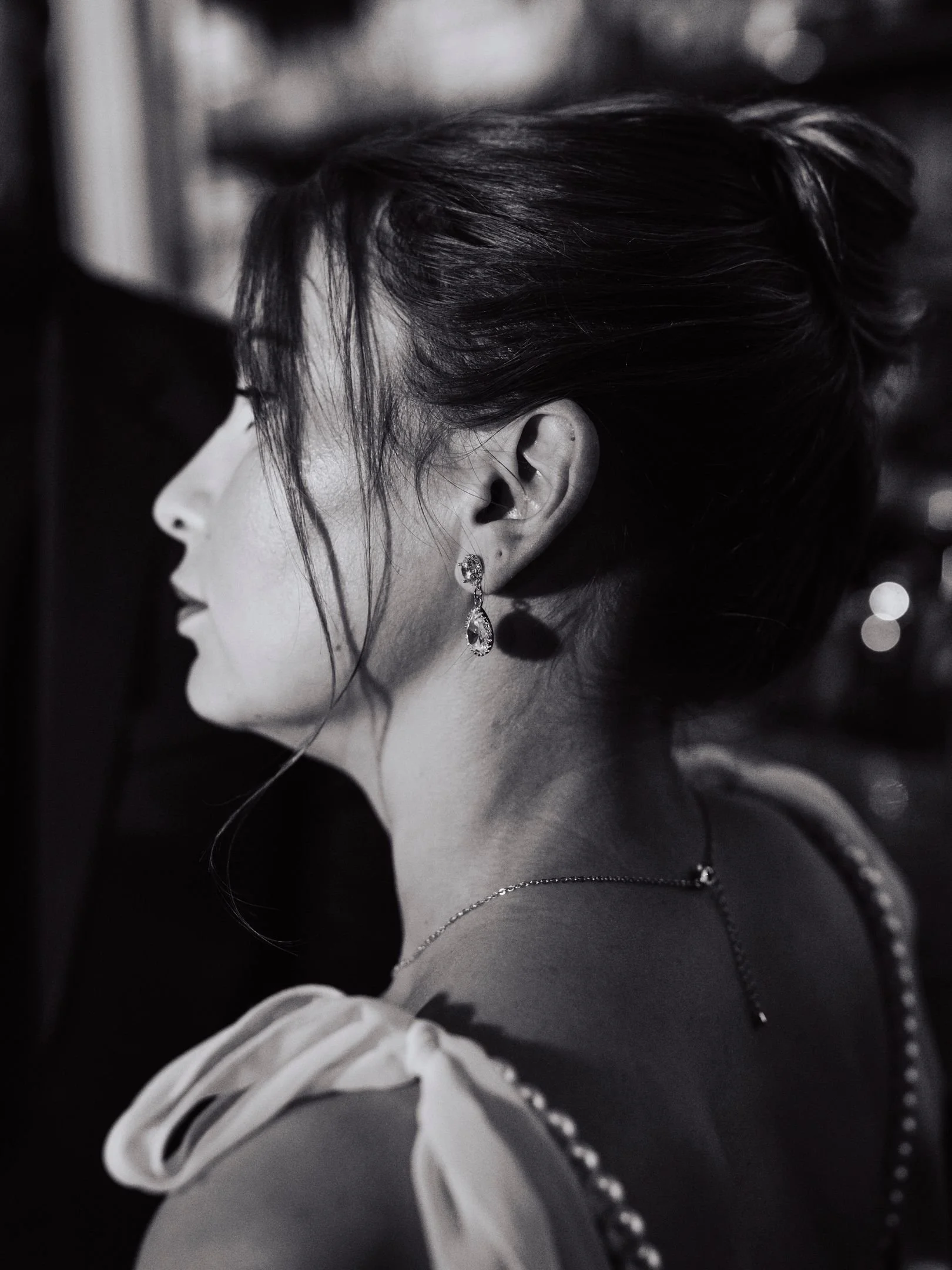 Portrait en noir et blanc d'une femme vue de profil avec des boucles d'oreilles pendantes et un collier, portant une robe avec des détails en perles, ses cheveux relevés.
