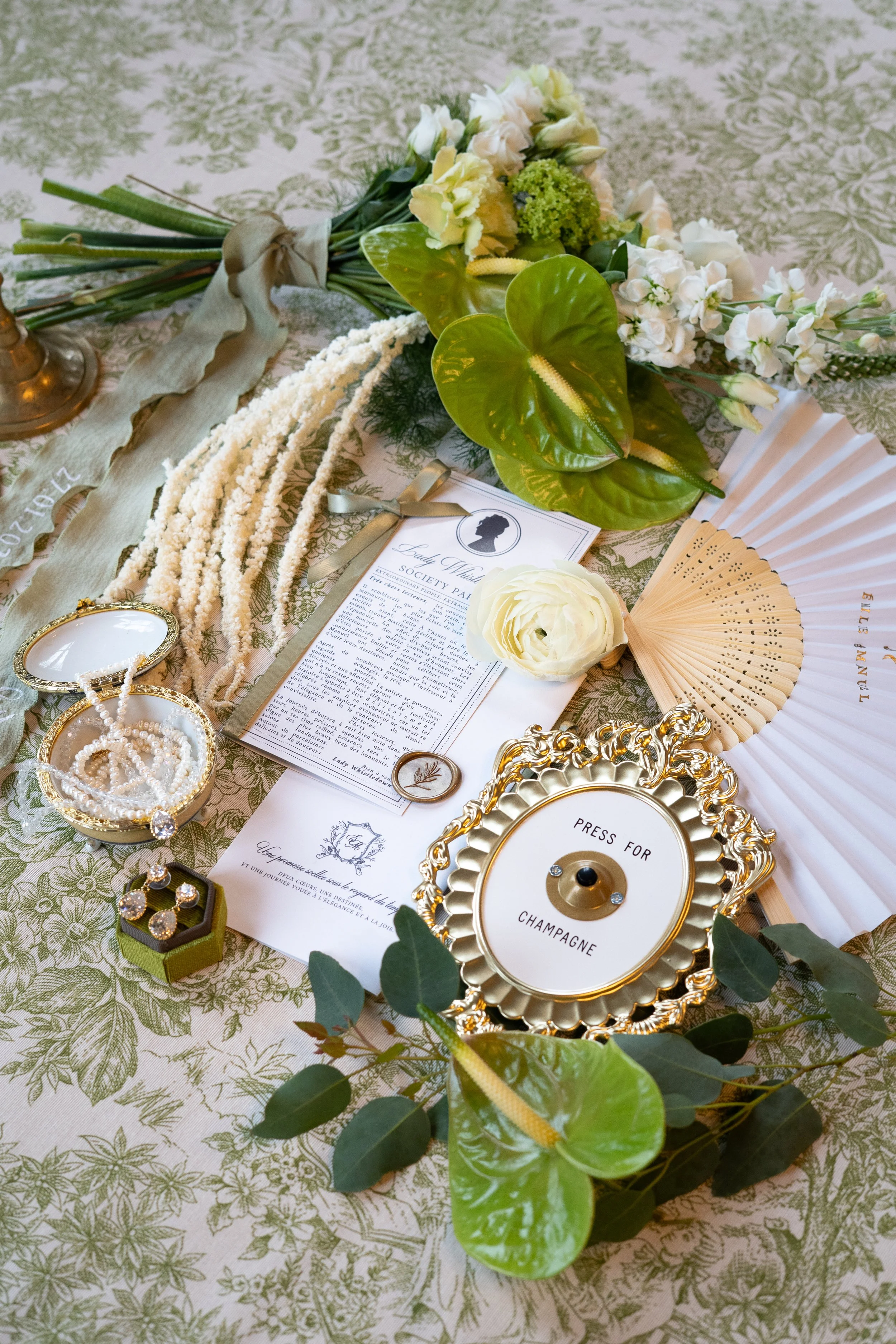 Décor de table avec fleurs, bijoux, un éventail en bois, un presse-papiers pour le champagne, et une invitation pour un évènement social