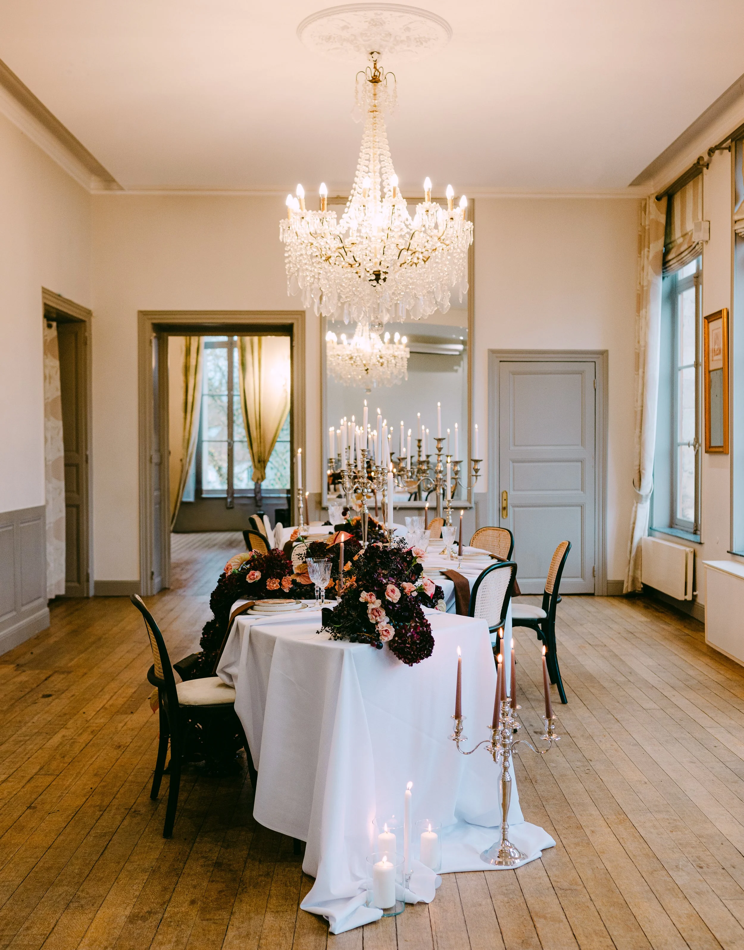 Salle à manger élégante avec chandeliers, fleurs et chandelles dans un décor sophistiqué avec lustre en cristal.