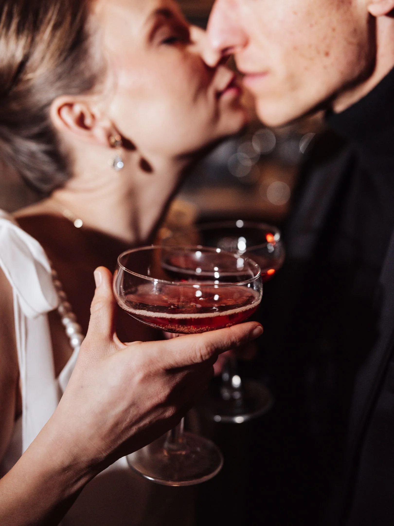Un couple s'embrasse en tenant des verres de vin rouge lors d'une célébration ou d'un événement romantique.