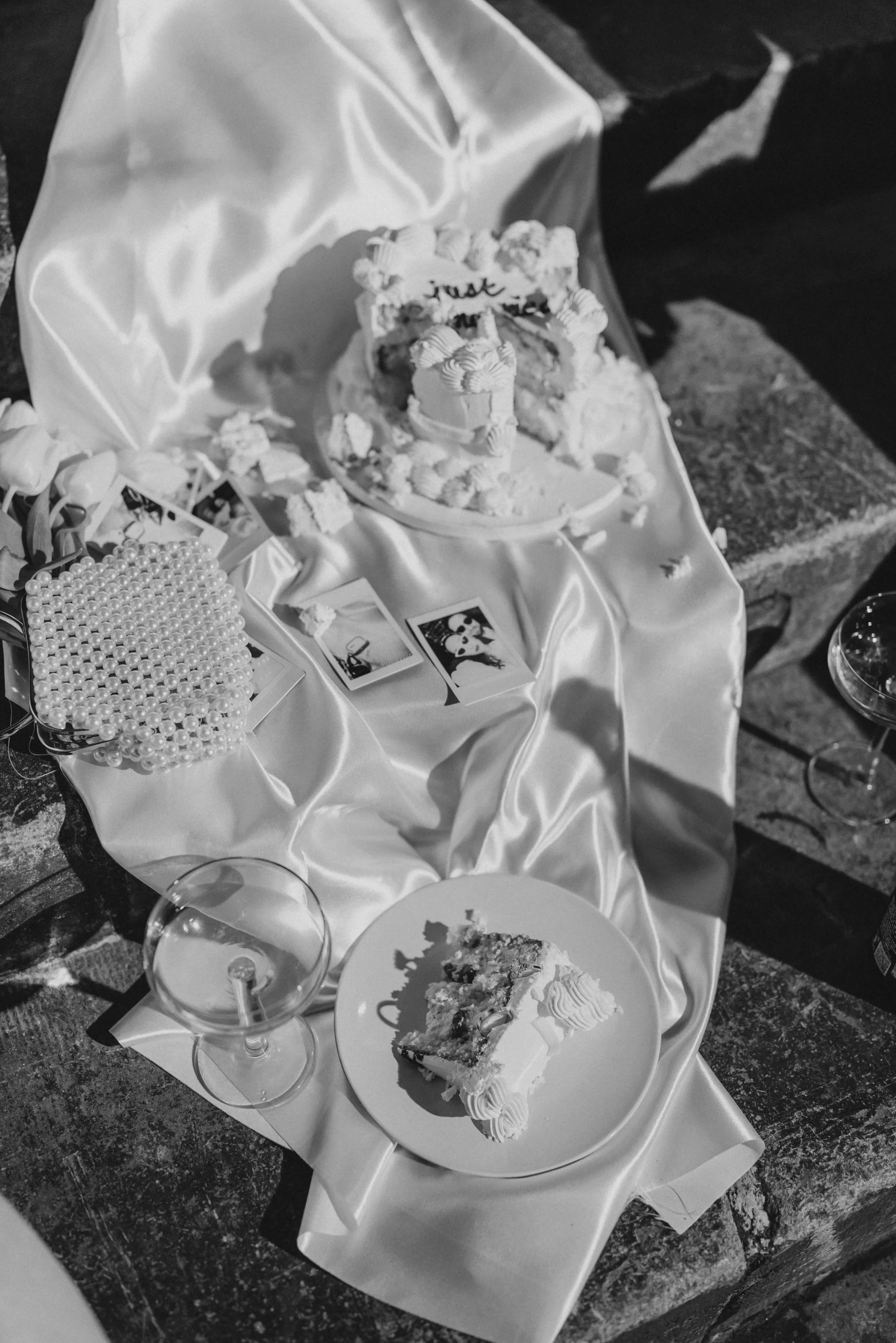 Une table avec une nappe en satin blanc, un gâteau de fête en partie mangé, une assiette avec une part de gâteau, des photos et un bracelet en perles blancs.